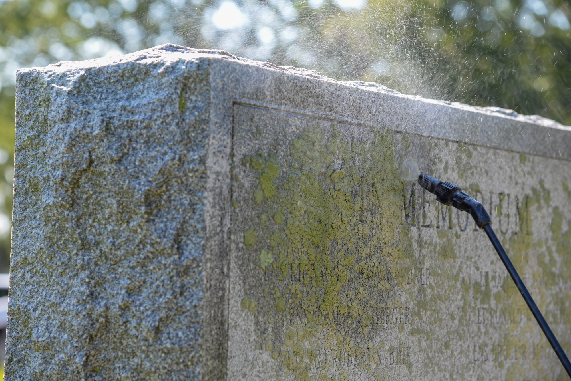 A picture of Melissa Swanson, Naval History and Heritage Command Conservator, spraying water on a U.S. Navy VC-4 memorial marker.