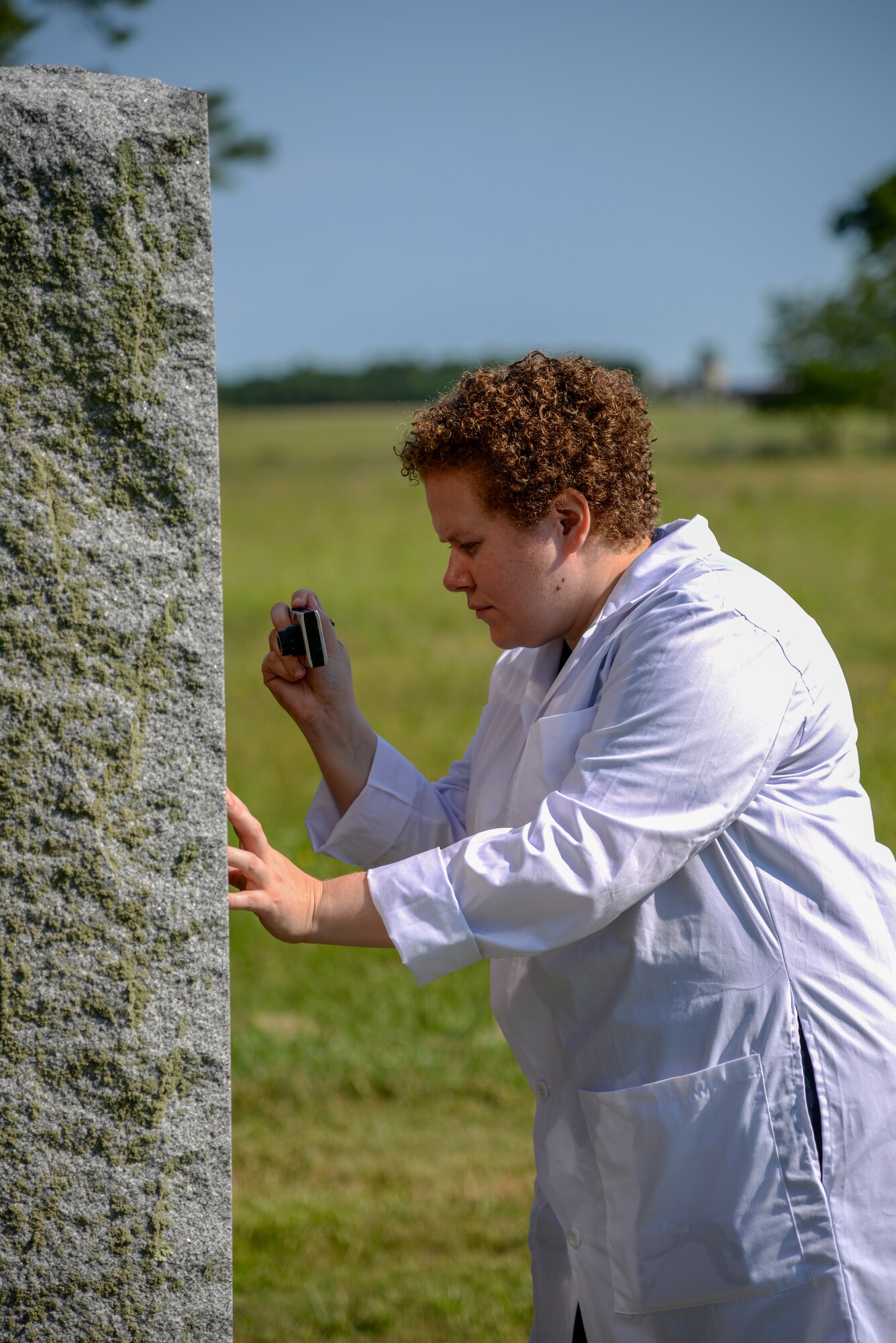 A picture of Melissa Swanson, Naval History and Heritage Command Conservator, taking a close up photo of a U.S. Navy VC-4 memorial marker.