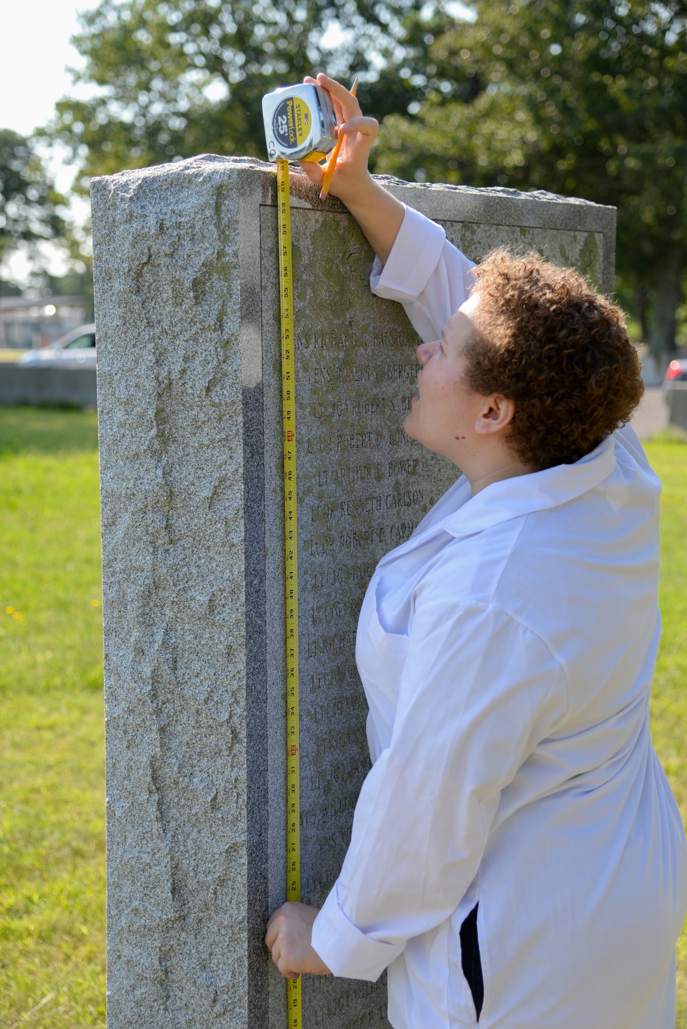 A picture of Melissa Swanson, Naval History and Heritage Command Conservator, taking measurements of a U.S. Navy VC-4 memorial marker.
