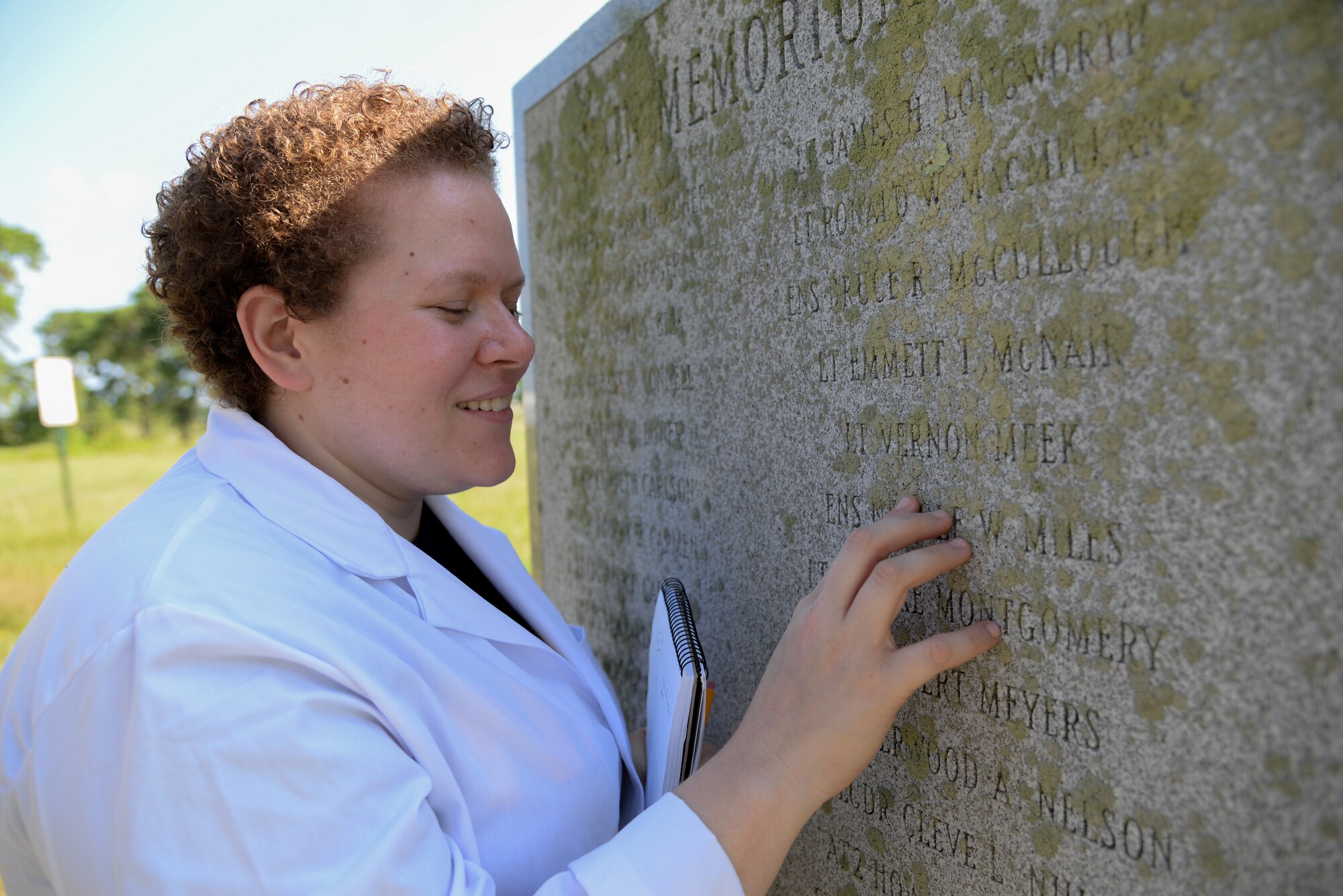A picture of Melissa Swanson, Naval History and Heritage Command Conservator, checking the condition of a U.S. Navy VC-4 memorial marker.