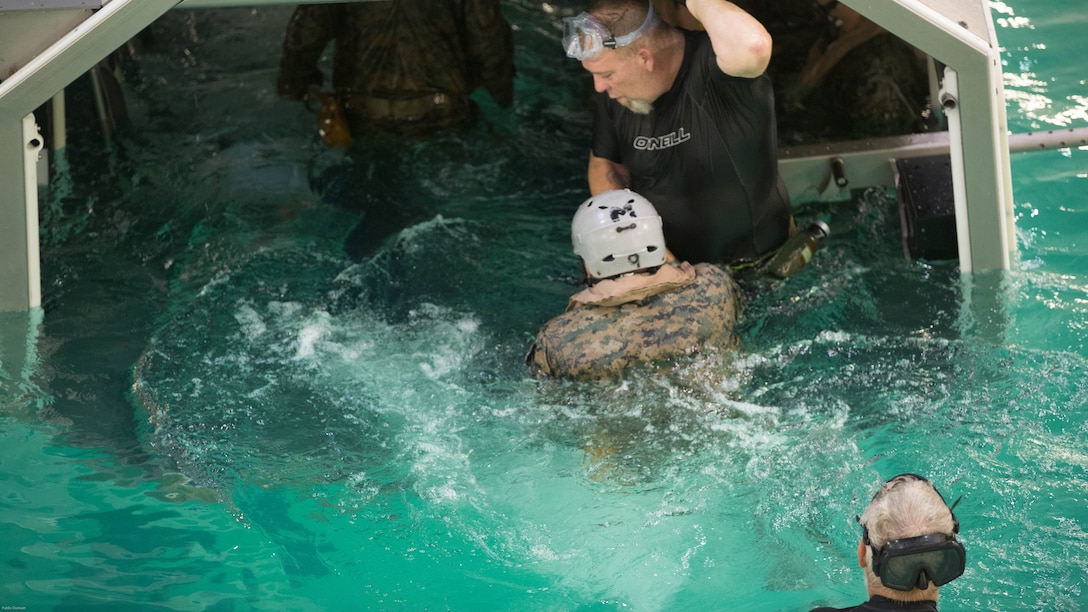 Jerry Blakenship an instructor with the Water Survival training facility aids a Marine into the Helo Dunker to begin his egress training at the Water Survival training facility on Marine Corps Base Camp Lejeune Aug. 5, 2016. The Marines undertook the training which is designed as a lifesaving course that provides service members with the skills and confidence too successfully and safely egress out of a helicopter that has suffered a controlled or uncontrolled landing within a body of water. 