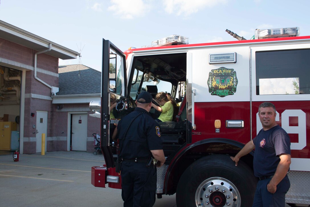 A DLA police officer helps a child explore a fire truck at Defense Distribution Center Susquehanna’s National Night Out.