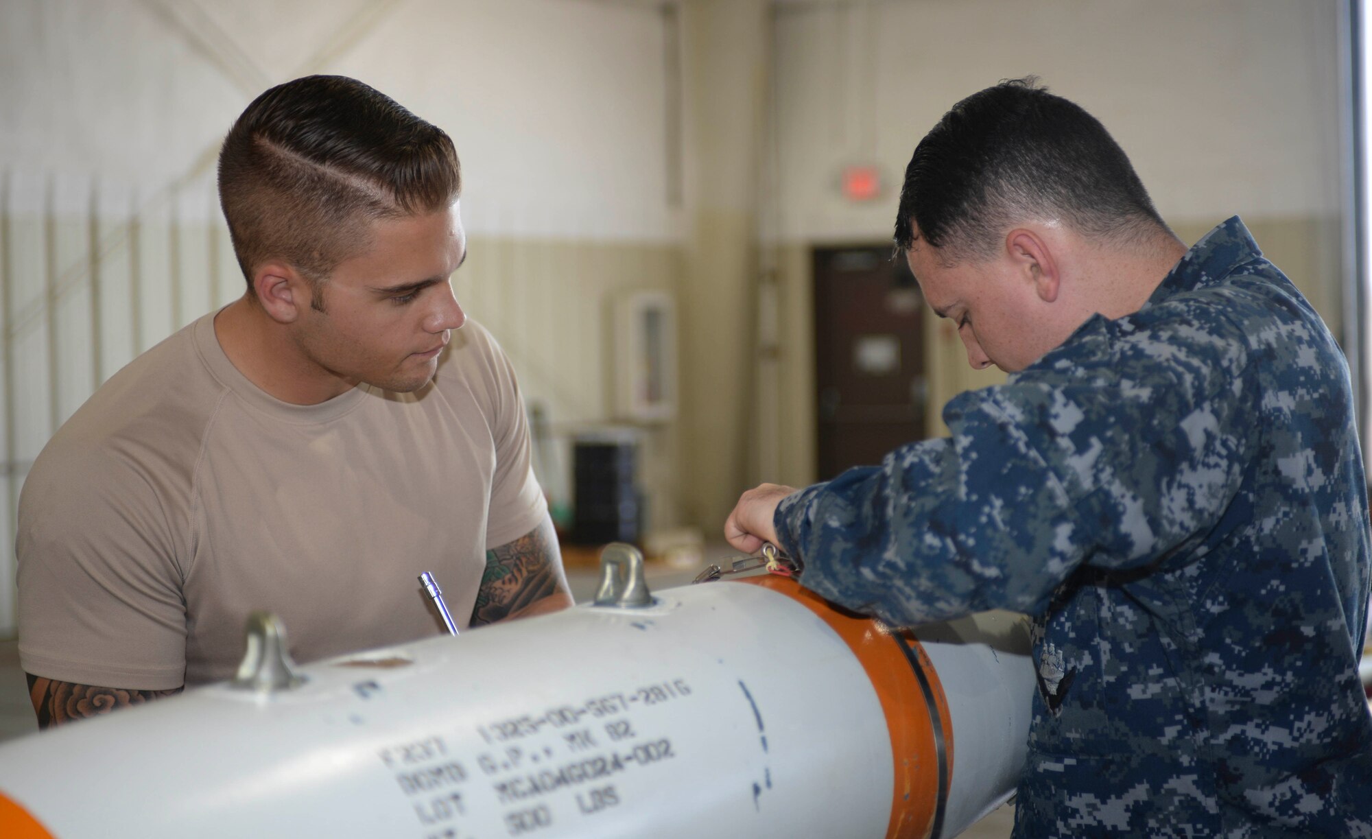 Senior Airman Justin Moyle, a conventional maintenance crew chief assigned to the 28th Munitions Squadron, observes Seaman Mathew King, a mineman assigned to the Navy Munitions Command Atlantic Unit, Charleston, S.C., as he builds an inert MK 62 mine at Ellsworth Air Force Base, S.D., July 20, 2016. Sailors conducted joint training with Ellsworth Airmen in July, instructing them on building mines that can be employed by the B-1 bomber. (U.S. Air Force photo by Airman 1st Class Sadie Colbert)