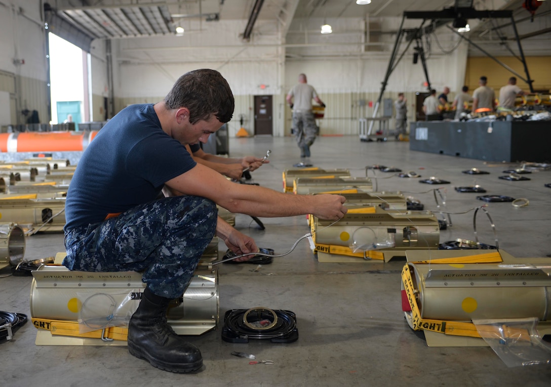 Seaman Apprentice Nicholas Deangelo, a mineman assigned to the Navy Munitions Command Atlantic Unit, Charleston, S.C., connects a lanyard to a pin on the fin of an inert MK 62 mine at Ellsworth Air Force Base, S.D., July 20, 2016. During an instructing course, several Airmen and Sailors worked together to create approximately 60 mines to be used in training in the future. (U.S. Air Force photo by Airman 1st Class Sadie Colbert)