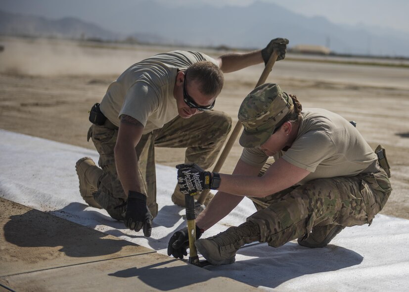 Master Sgt. Cassandra Doub, 455th Expeditionary Civil Engineer Squadron 1st Sgt., and Staff Sgt. Andrew Perna, 455th Expeditionary Civil Engineer Squadron maintenance and equipment craftsman secure AM-2 matting with a hammer, Bagram Airfield, Afghanistan, Aug. 11, 2016. AM-2 matting is used to form runways, taxiways, parking and other areas required for aircraft operations and maintenance. In an effort to create a drive way for aircraft, the ECES laid an estimated 49 thousand square feet of matting on the flightline. The additional matting will allow pilots to have a faster response time. (U.S. Air Force photo by Senior Airman Justyn M. Freeman)