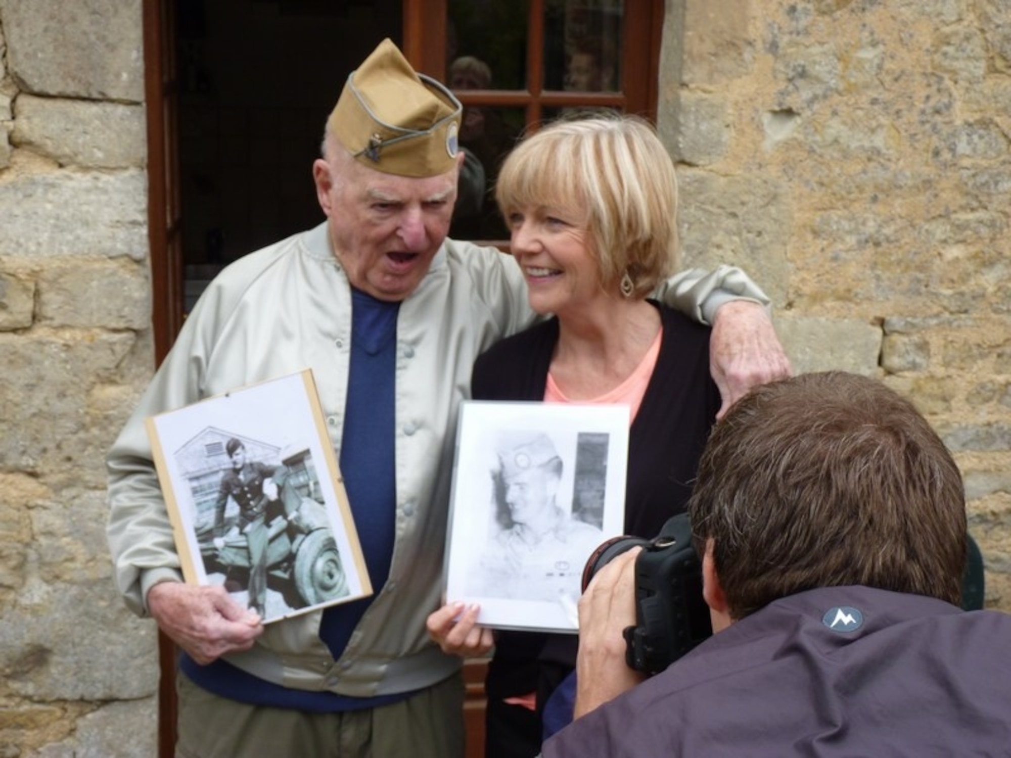 William “Bill” Sullivan and wife, Elizabeth, hold up old photos of Bill at a reunion celebration in Normandy, France. The photos are from his time in service as a prisoner of war during World War II 1944-1945. (Courtesy Photo)