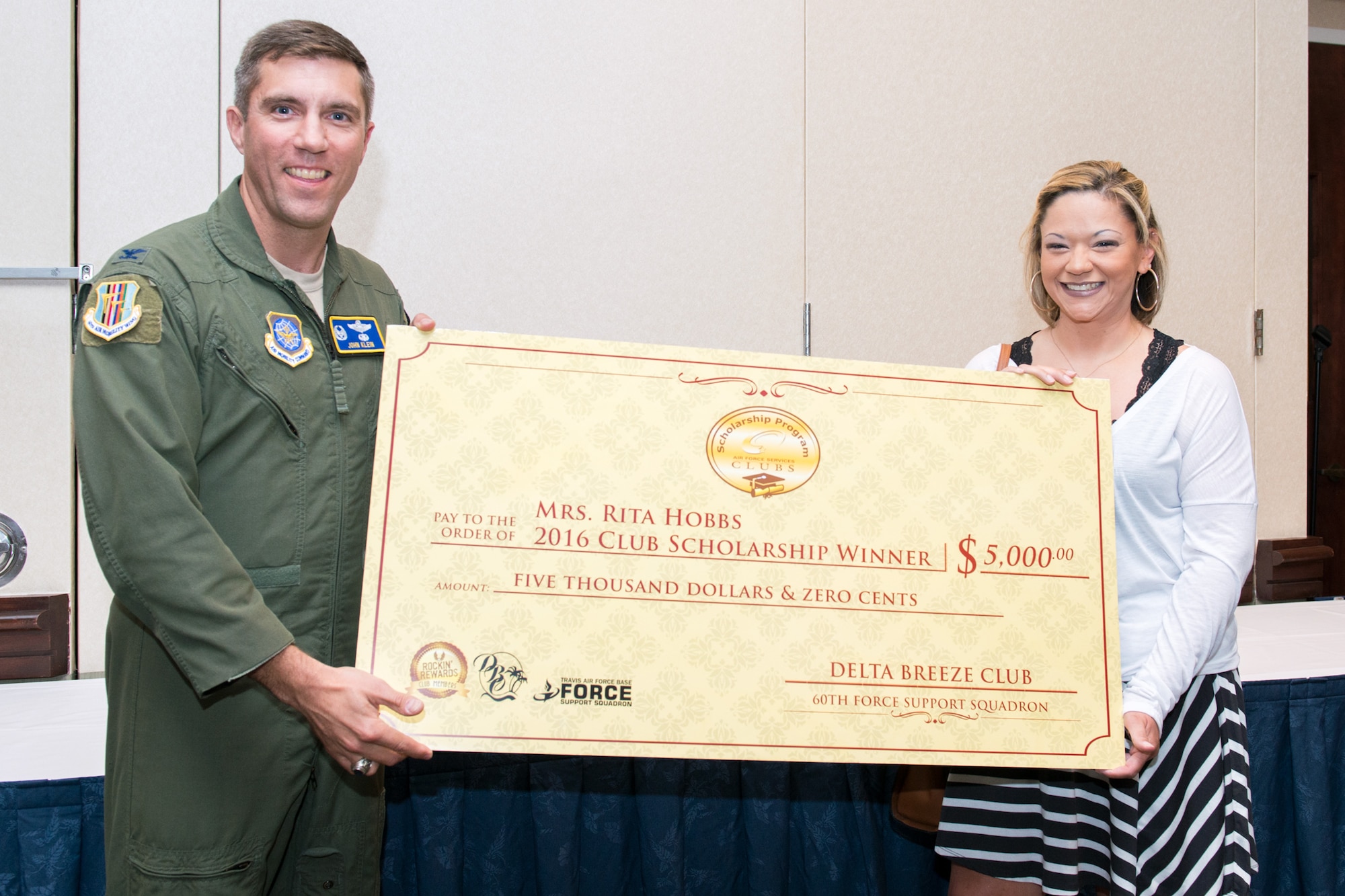 Col. John Klein, 60th Air Mobility Wing commander, presents Rita Hobbs with a scholarship check for $5,000 at Travis Air Force Base, Calif., Aug. 5, 2016. Hobbs, the dependent of Master Sgt. Dave Hobbs, 621st Contingency Response Support Squadron, won the scholarship for her essay, "One Heck of a Ride," which took first place in the club member scholarship competition. (U.S. Air Force photo by Louis Briscese)    