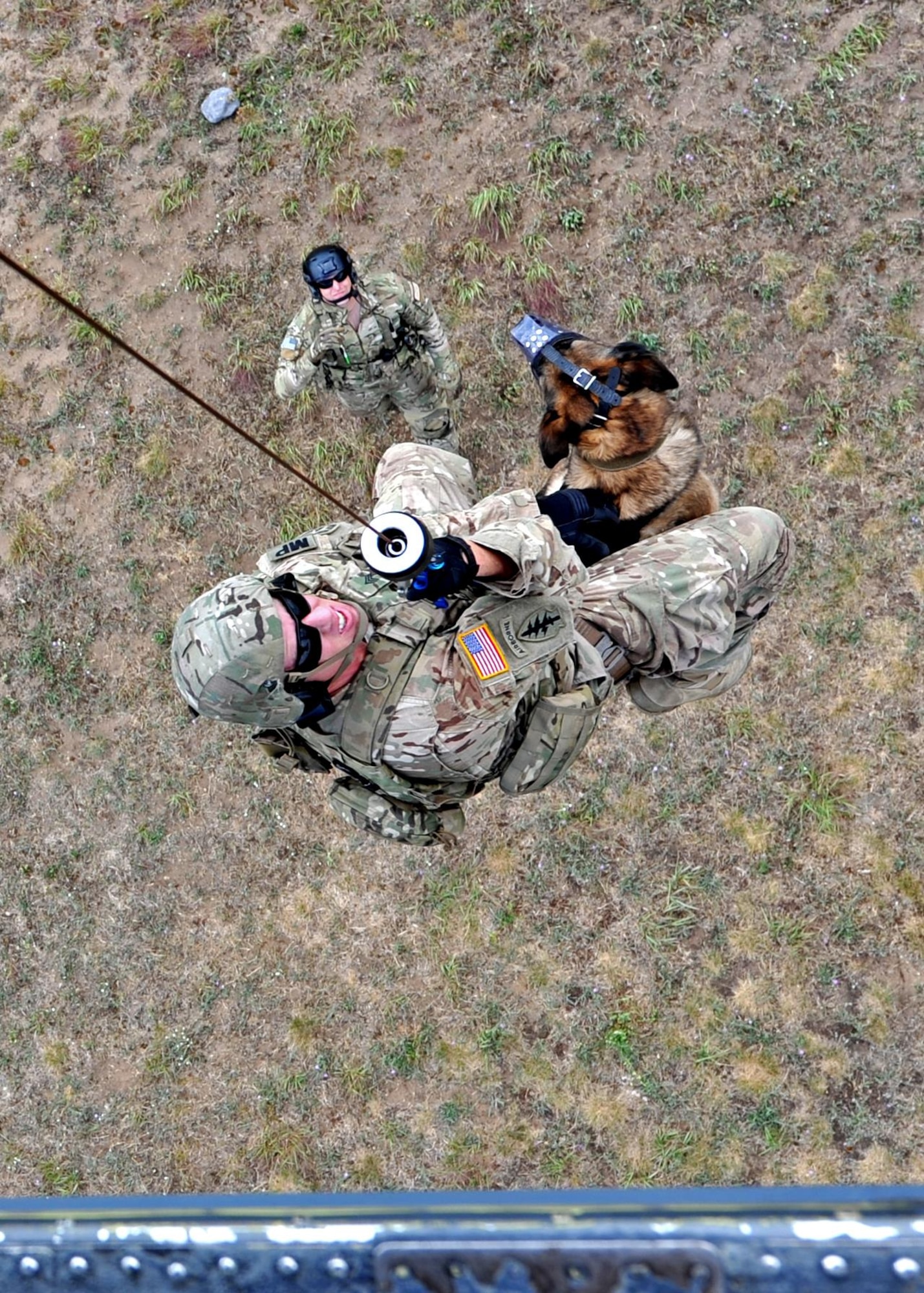 A K-9 handler from the 8th Military Police Detachment, 91st Military Police Battalion, hangs on as he's hoisted with his working dog into a 305th Rescue Squadron HH-60 Aug. 3 at Fort Drum, NY, while Tech. Sgt. Gary Waltz, a 306th Rescue Squadron Survive, Evade, Resist, Escape (SERE) specialist, assists from the ground. Approximately 50 Air Force Reserve Airmen from the 943rd Rescue Group deployed for training to the East coast for joint operations July 31 to Aug 12. (U.S. Air Force photo by Carolyn Herrick)
