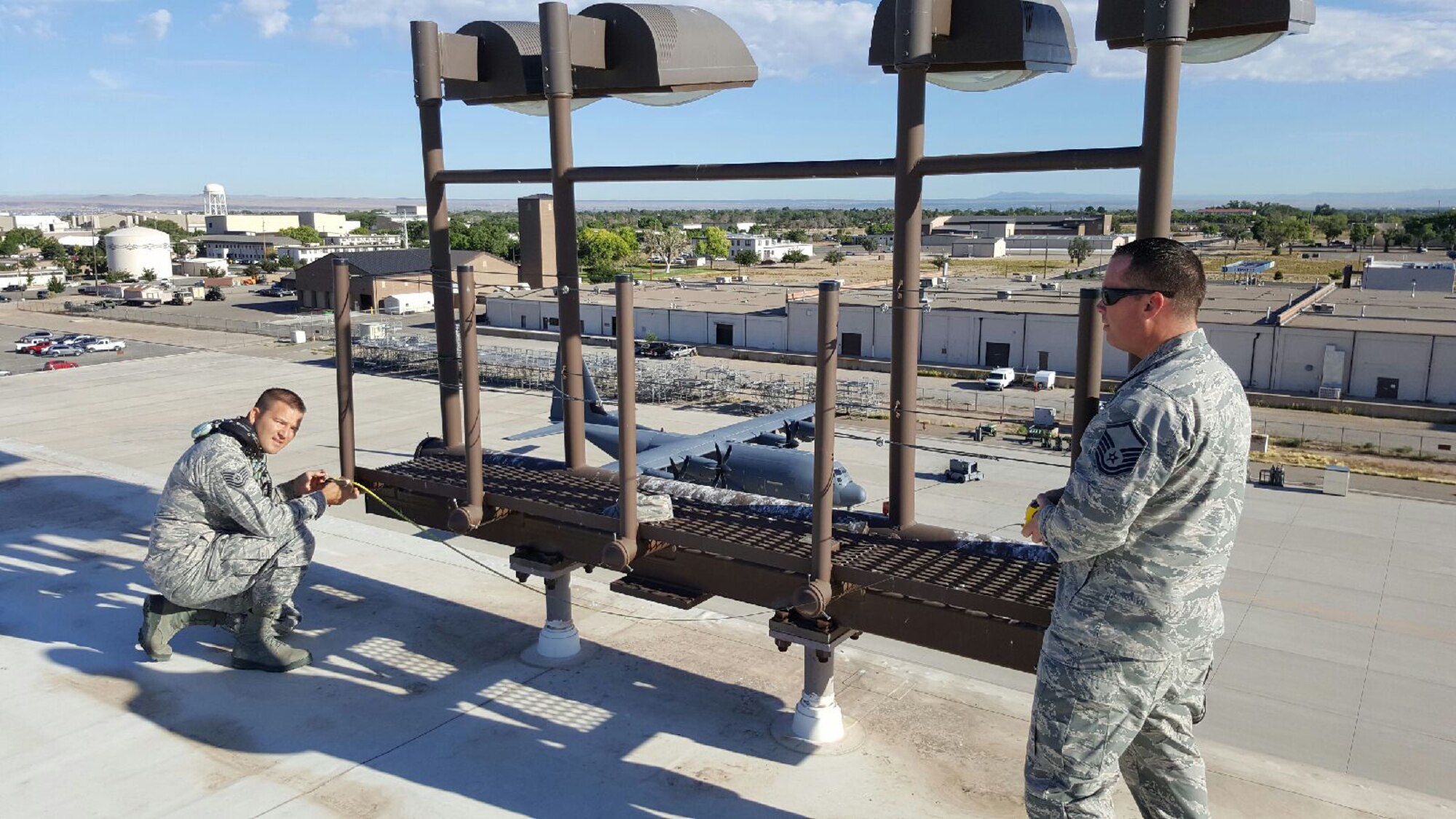 Tech. Sgt Michael Altigieri and Master Sgt. Timothy "Sax" Saxongwara, both from the 58th Special Operations Wing, measure structural dimensions on one of the existing light fixtures on Hangar 1002. Kirtland could become a test site for cutting-edge LED lighting that would save the Department of Defense thousands of dollars. 