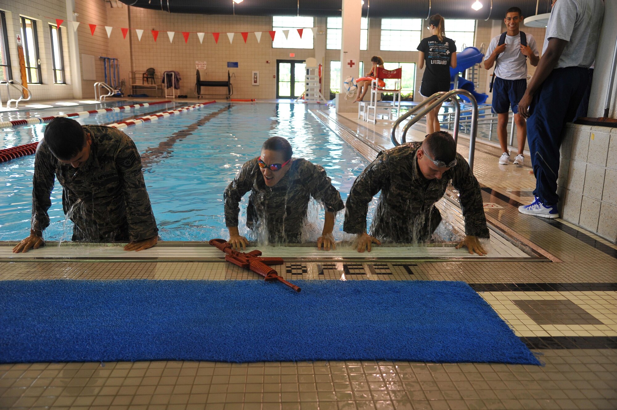 Airmen from the 319th Medical Group participate in the combat swim event during Summer Bash, August 12, 2016 on Grand Forks Air Force Base, N.D. A team of three swim in ABUs, while holding a simulated rifle from one end of the pool to the other. (U.S. Air Force Photo by A1C Elijaih Tiggs/released)