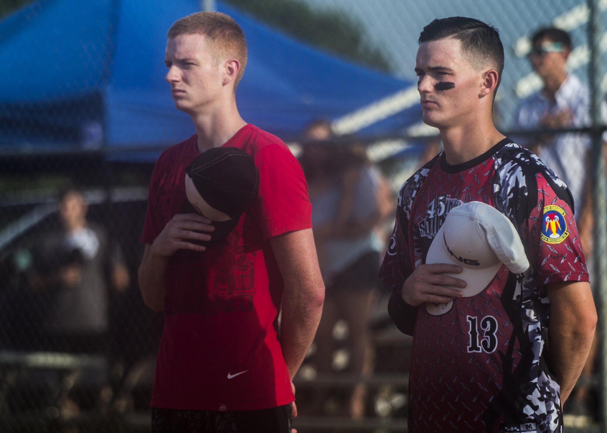 U.S. Air Force Airman 1st Class Steven, left, and Senior Airman Doug, 30th Intelligence Squadron imagery analysts, watch the presentation of colors by the Langley Honor Guard before the start of the 2016 Intramural Softball Championship at Langley Air Force Base, Va., Aug. 10, 2016. The 30th IS faced off against the 438th Special Operations Group to determine the Langley intermural softball champion team.(U.S. Air Force photo by Airman 1st Class Kaylee Dubois)
