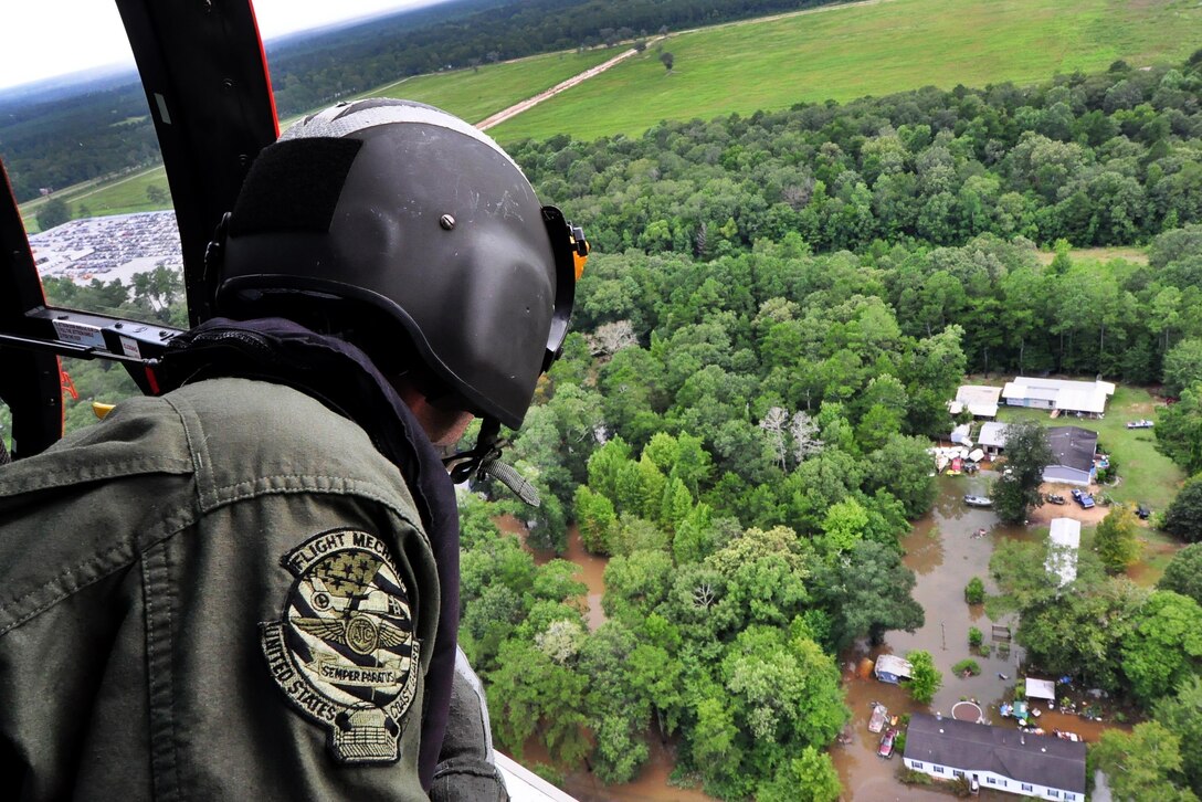 A Coast Guardsman looks out from an MH-65 Dolphin helicopter searching for stranded residents in Baton Rouge, La., Aug. 15, 2016. The guardsman is an aviation maintenance technician assigned to Air Station New Orleans. Coast Guard photo by Petty Officer 1st Class Melissa Leake