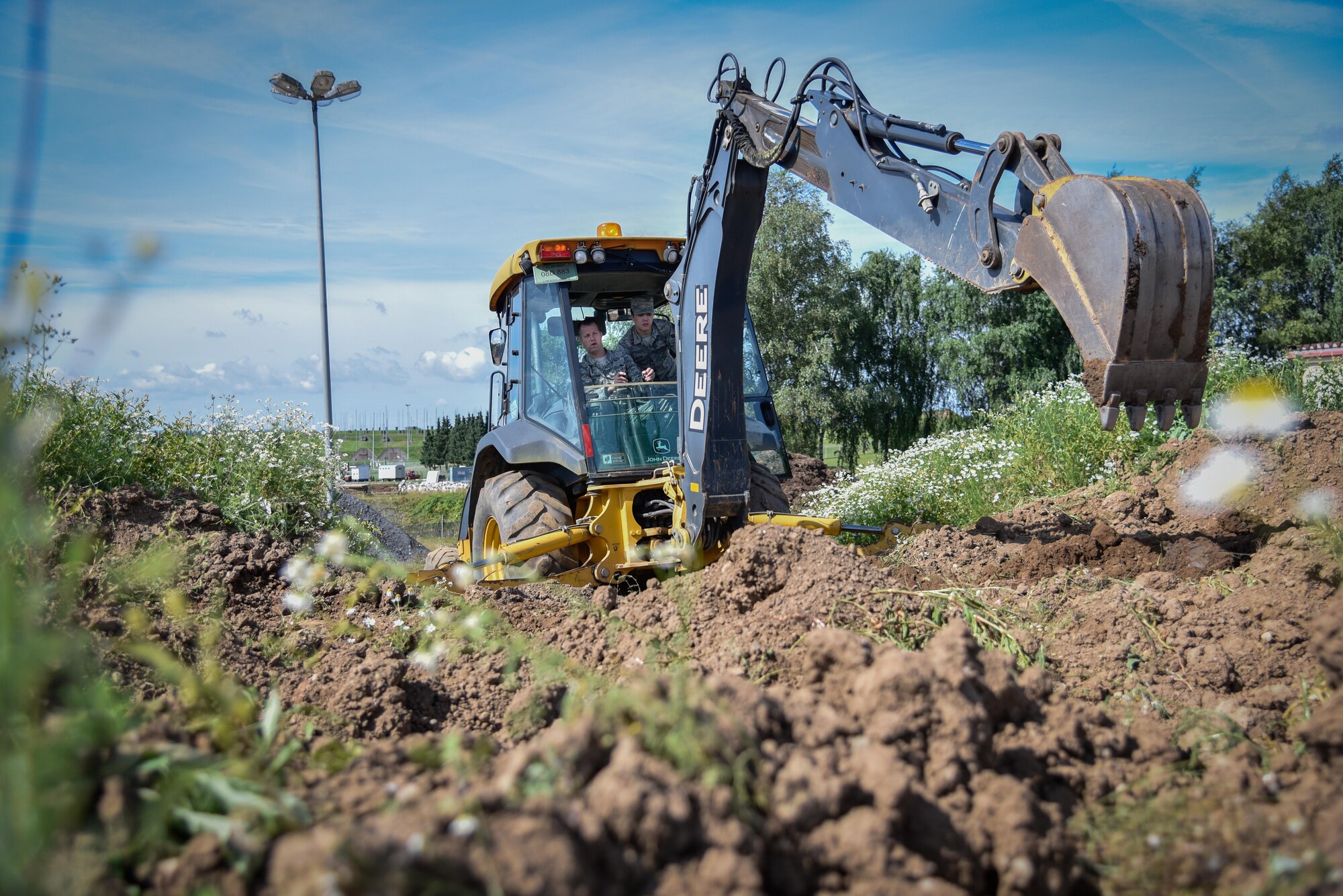 Chief Master Sgt. Edwin Ludwigsen, 52nd Fighter Wing command chief, uses a backhoe to dig holes under the guidance of Airman 1st Class Justin Leyno, 52nd Civil Engineer Squadron heavy equipment operator, during an “out and about” visit at Spangdahlem Air Base, Germany, Aug. 11, 2016. (U.S. Air Force photo by Tech. Sgt. Christopher Parr)