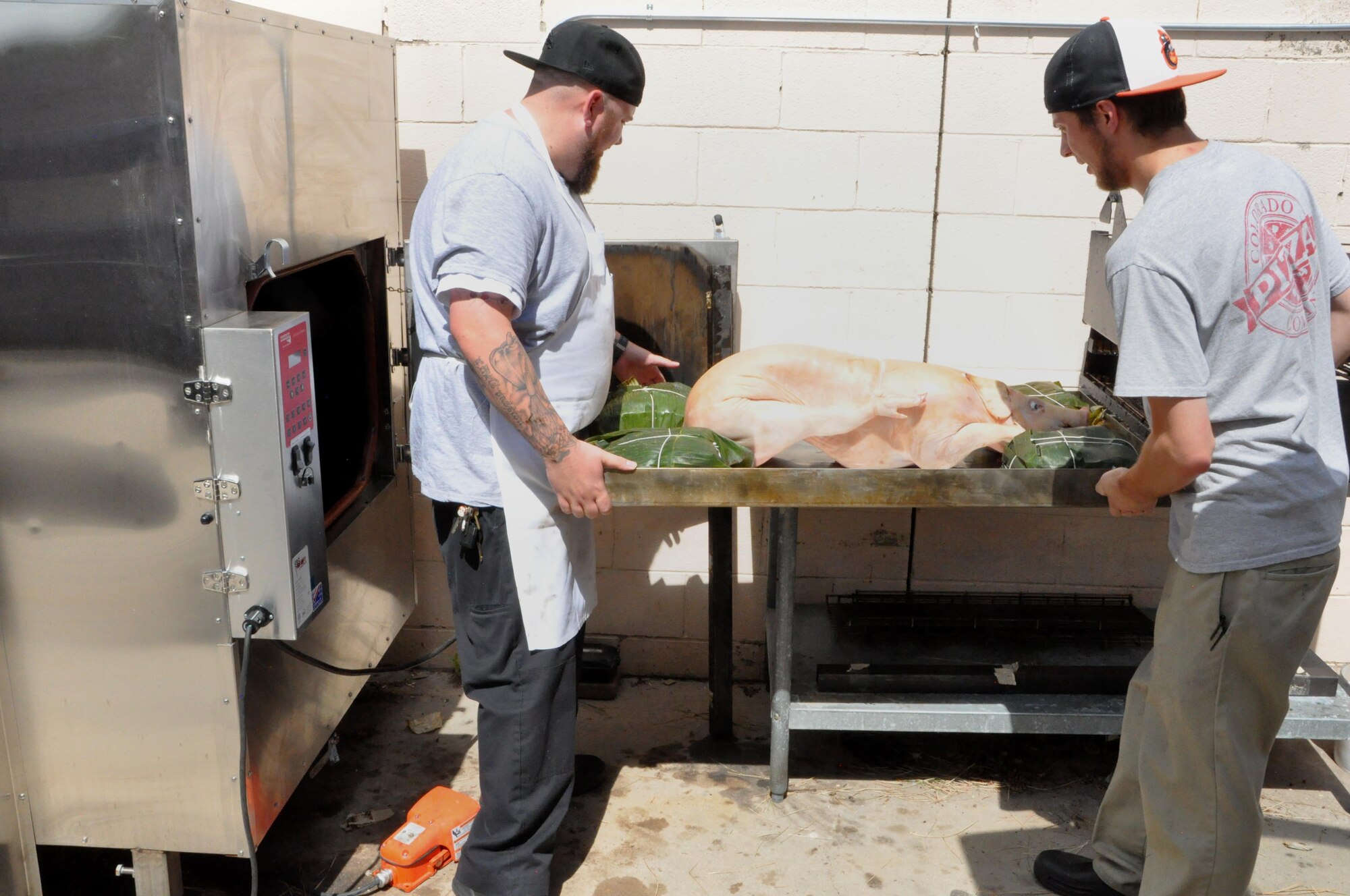 Chef Kirkland Dunning (left), and Jeremy Long, sous chef, put a 44-pound pig into the smoker Aug. 10, 2016, at the Greenside Grill and Smokehouse. The smoker can hold up to 300 pounds of meat, and delivers patrons a hickory-smoked lunchtime dining option. The newly remodeled restaurant re-opened in April, offering fresh, unique lunch choices with a decidedly smoky flavor. (U.S. Air Force photo by Steve Brady)