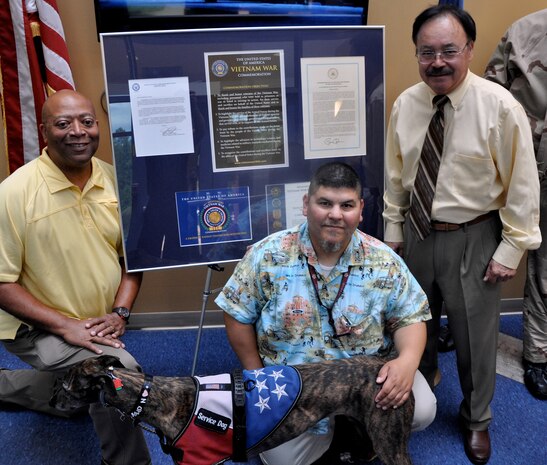 DAHLGREN - Marietto Jeffries, Naval Surface Warfare Center Dahlgren Division (NSWCDD) Vietnam Memorial Commemoration coordinator; Nelson Zapata, an NSWCDD engineer and Marine Corps veteran; and Udo Goff, an NSWCDD defense contractor who is a Vietnam veteran and retired Navy commander, stand left to right with Zapata's service dog, Fallon, at the NSWCDD Vietnam Memorial Commemoration display in the Herbert H. Bateman Chemical Biological Defense Center, Aug. 1.