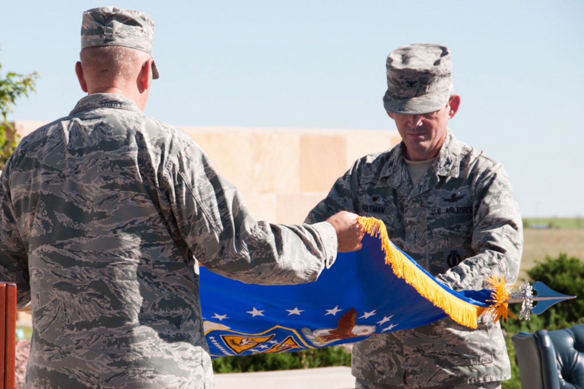 Col. Damon Feltman, 310th Space Wing commander, and Col. Neal Landeen, 310th Mission Support Group commander unfurl the Mission Support Group colors to be placed in the unit’s new home at the 310th Space Wing Headquarters building on Schriever AFB, Colo., Aug. 7, 2016.