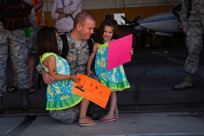 An Airman from the 4th Space Control Squadron holds his daughters and looks at the signs they made for him on the flightline at Peterson Air Force Base, Colo., Aug. 13, 2016. The unit just returned from deployment and rushed to meet their waiting families. (U.S. Air Force photo by Senior Airmen Rose Gudex)