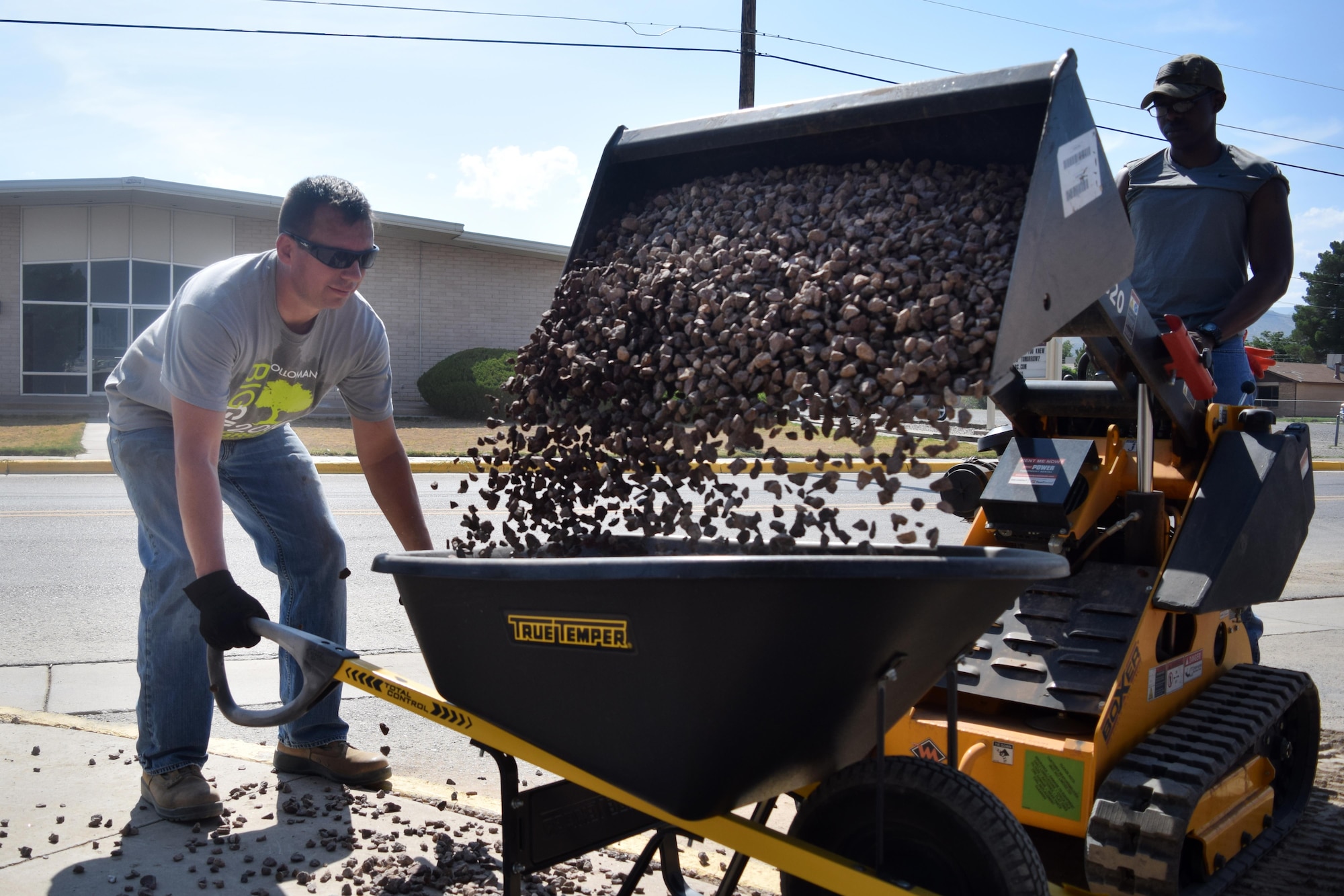 Volunteers dump of load of rock into a wheel barrow during a beautification project at Sierra Elementary School in Alamogordo, N.M., on July 30, 2016. The team spent a total of 234 man hours, during six separate days finishing the task. (U.S. Air Force photo by Staff Sgt. Eboni Prince)