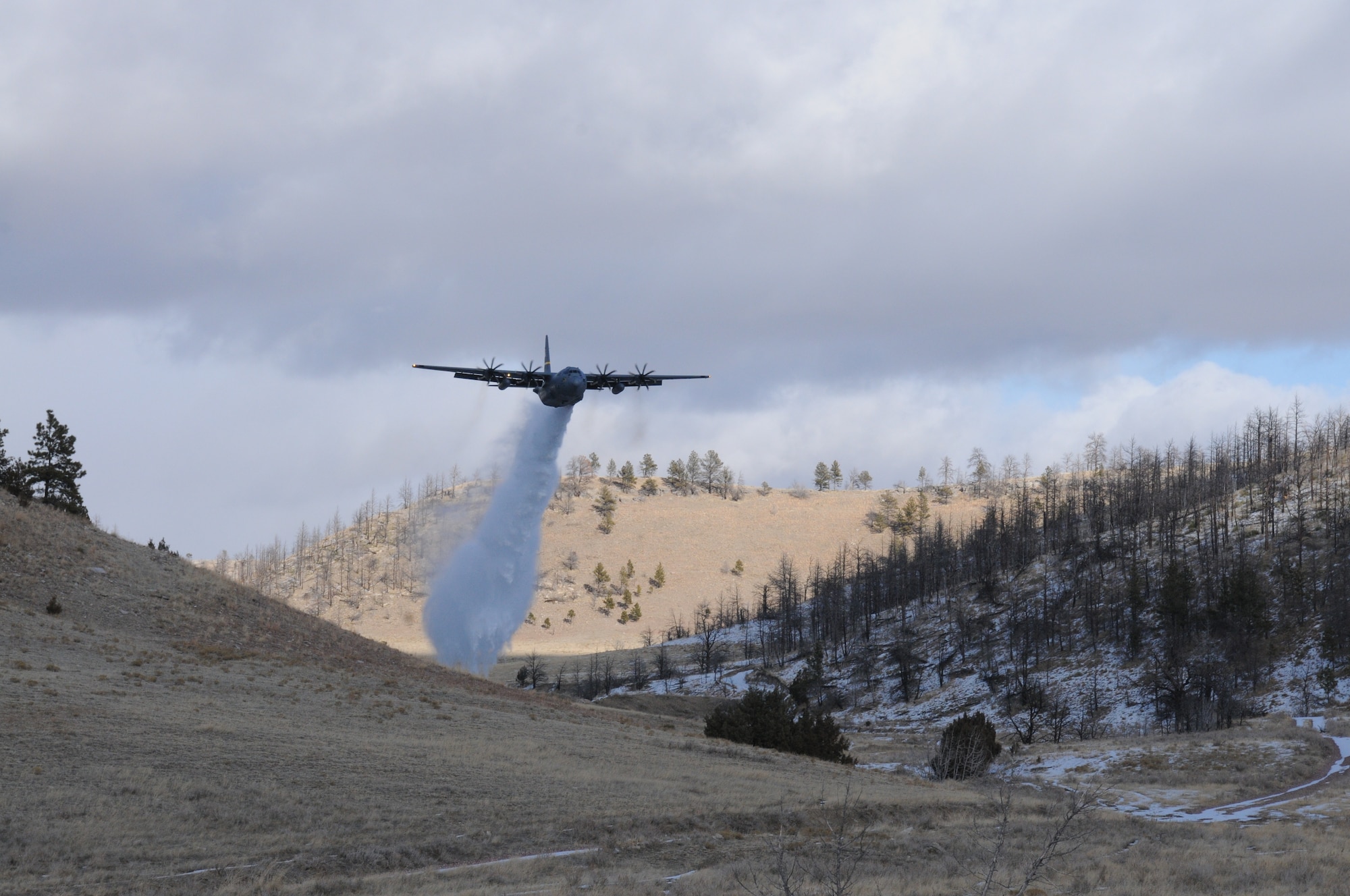 A C-130H Hercules aircraft assigned to the 153rd Airlift Wing, Wyoming Air National Guard sprays water over Camp Guernsey, Wyoming during Modular Airborne Fire Fighting System training. The training is being performed using a C-130 modified with an Electronic Propeller Control System and eight-bladed propeller system. (Courtesy photo)