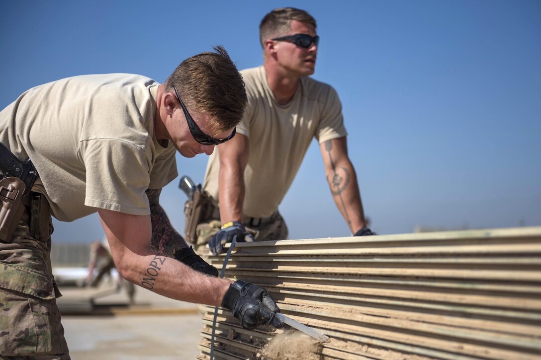 Air Force Senior Airman Seth Lindquist, left, removes dirt from a piece of aluminum matting during a ramp expansion project at Bagram Airfield in Afghanistan, Aug. 11, 2016. Lindquist, an operations management technician, is assigned to the 455th Expeditionary Civil Engineer Squadron. Air Force photo by Senior Airman Justyn M. Freeman