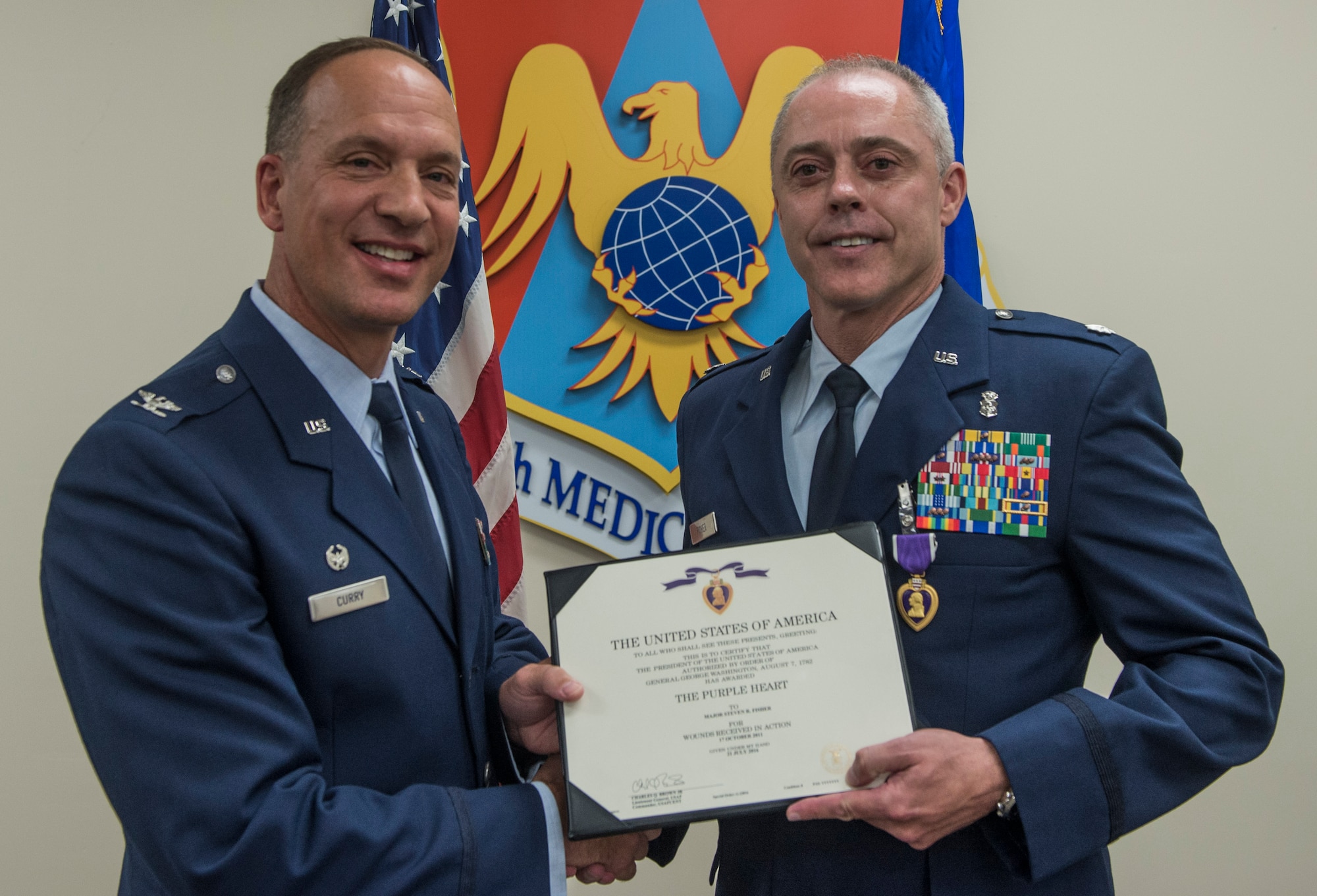 Col. Douglas Curry, 375th Medical Group commander presents Lt. Col. Steven Fisher with the Purple Heart during a ceremony on Aug. 12, 2016 at Scott Air Force Base, Ill. On Oct. 17, 2011 Fisher was injured in the line of duty during a rocket attack while deployed to Afghanistan. (U.S. Air Force Photo by Airman Daniel Garcia)