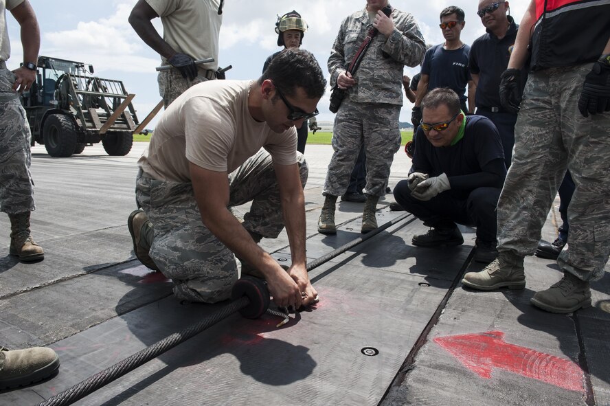 Staff Sgt. Fardad Alimehri, 18th Civil Engineer Squadron electrical power production and barrier maintenance technician, demonstrates how to properly secure an aircraft barrier cable Aug. 16, 2016, at Kadena Air Base, Japan. To ensure optimum performance of the cable when aircraft approach, it’s important to keep it properly aligned. (U.S. Air Force photo by Airman 1st Class Lynette M. Rolen)
