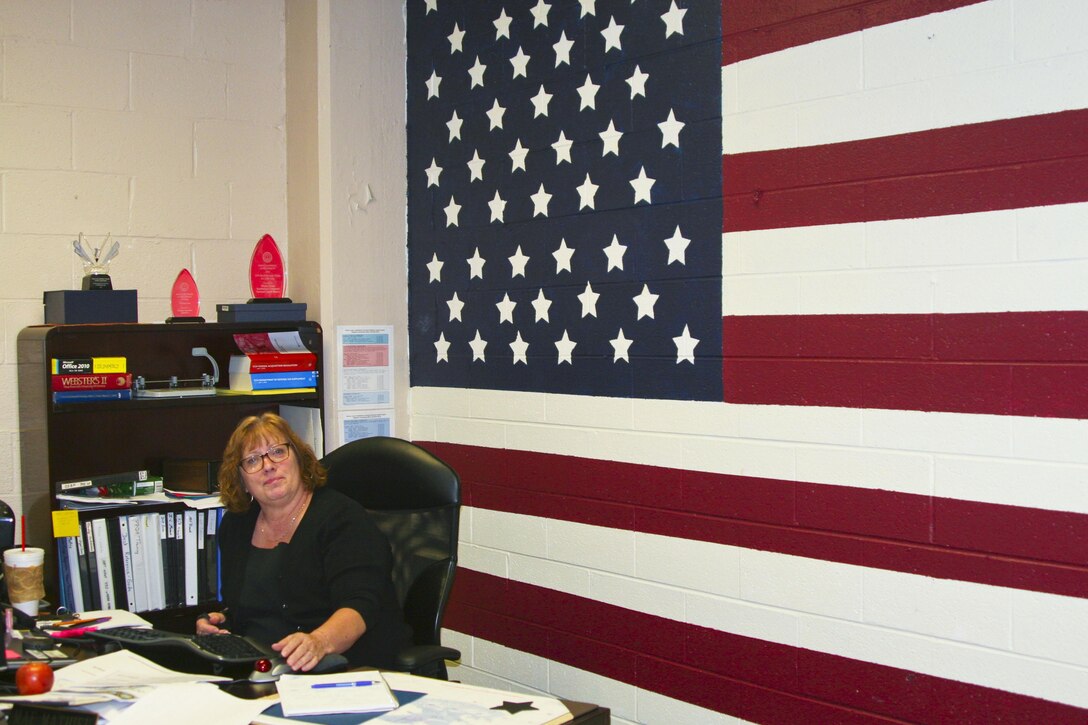Mae Mathieu sits in front of the 8-by-16 foot mural of the American flag she painted on her office wall.