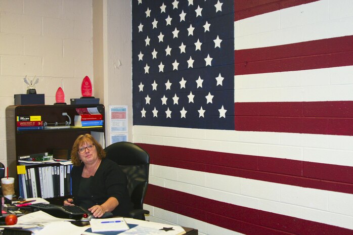 Mae Mathieu sits in front of the 8-by-16 foot mural of the American flag she painted on her office wall.