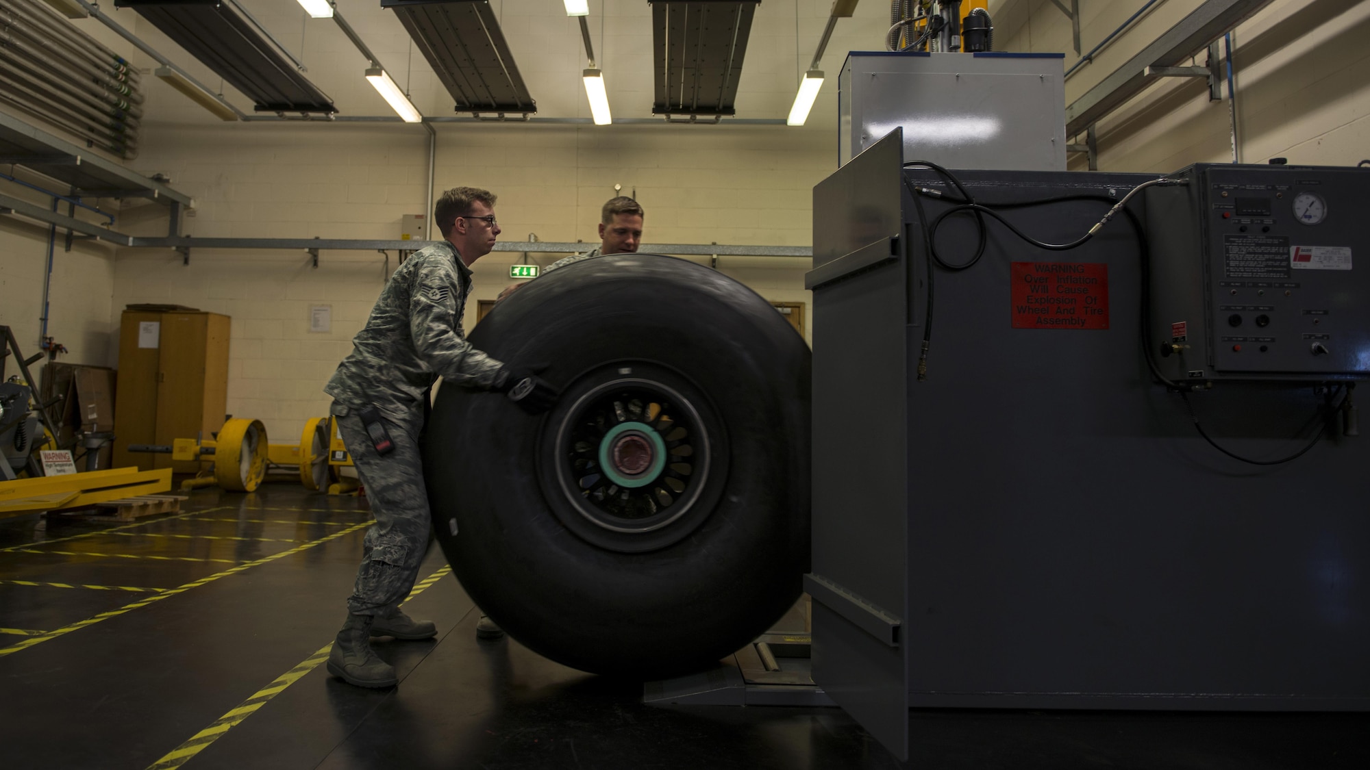 U.S. Air Force Staff Sgt. Michael Miller (left) and Tech. Sgt. Lance Moore (right), 352d Special Operations Aircraft Maintenance Squadron repair and reclamation technicians load an MC-130J Commando II carbon wheel into the tire inflator cage on RAF Mildenhall, England, Aug. 19, 2016. As they contain pressure well over 100 psi, aircraft tires need to be placed in a protective cage during inflation to ensure the safety of the maintainers who service them. (U.S. Air Force photo by 1st Lt Chris Sullivan/Released)