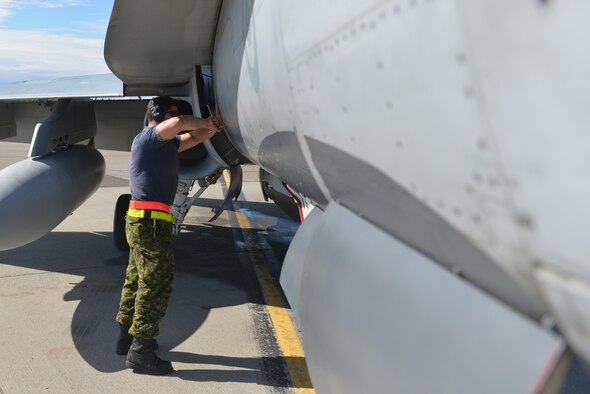 Royal Canadian Air Force Cpl. Zach McCann, an aviation systems technician assigned to the 409th Tactical Fighter Squadron out of Canadian Forces Base Cold Lake, Alberta, unscrews a hatch on the side of a CF-18 Hornet aircraft during RED FLAG-Alaska (RF-A) 16-3, at Eielson Air Force Base, Alaska,Aug. 18, 2016. RF-A provides training for deployed maintenance and support personnel in sustainment of large-force air operations. (U.S. Air Force photo by Airman Isaac Johnson)