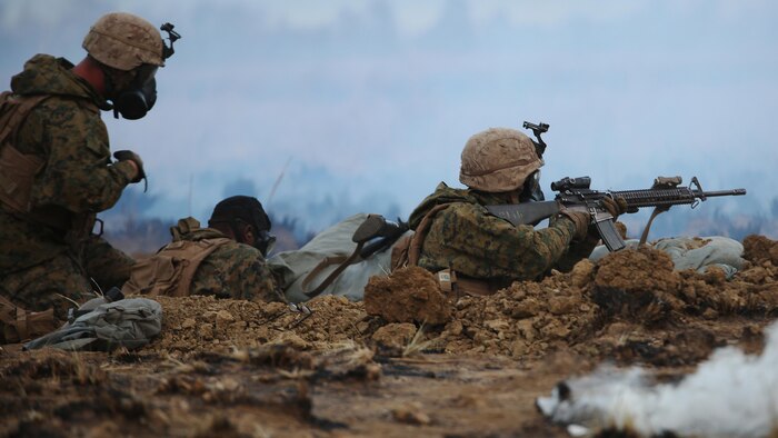 A Marine with 1st Battalion, 1st Marine Regiment provides security while another Marine puts on his gas mask during a CS gas attack August 18, 2016, at Bradshaw Field Training Area, Northern Territory, Australia. The range was the final training evolution of Exercise Koolendong 16, a trilateral exercise between the U.S. Marine Corps, Australian Defence Force and French Armed Forces New Caledonia. Marines held a defensive position while engaging targets and working through the CS gas, which simulated a chemical attack.