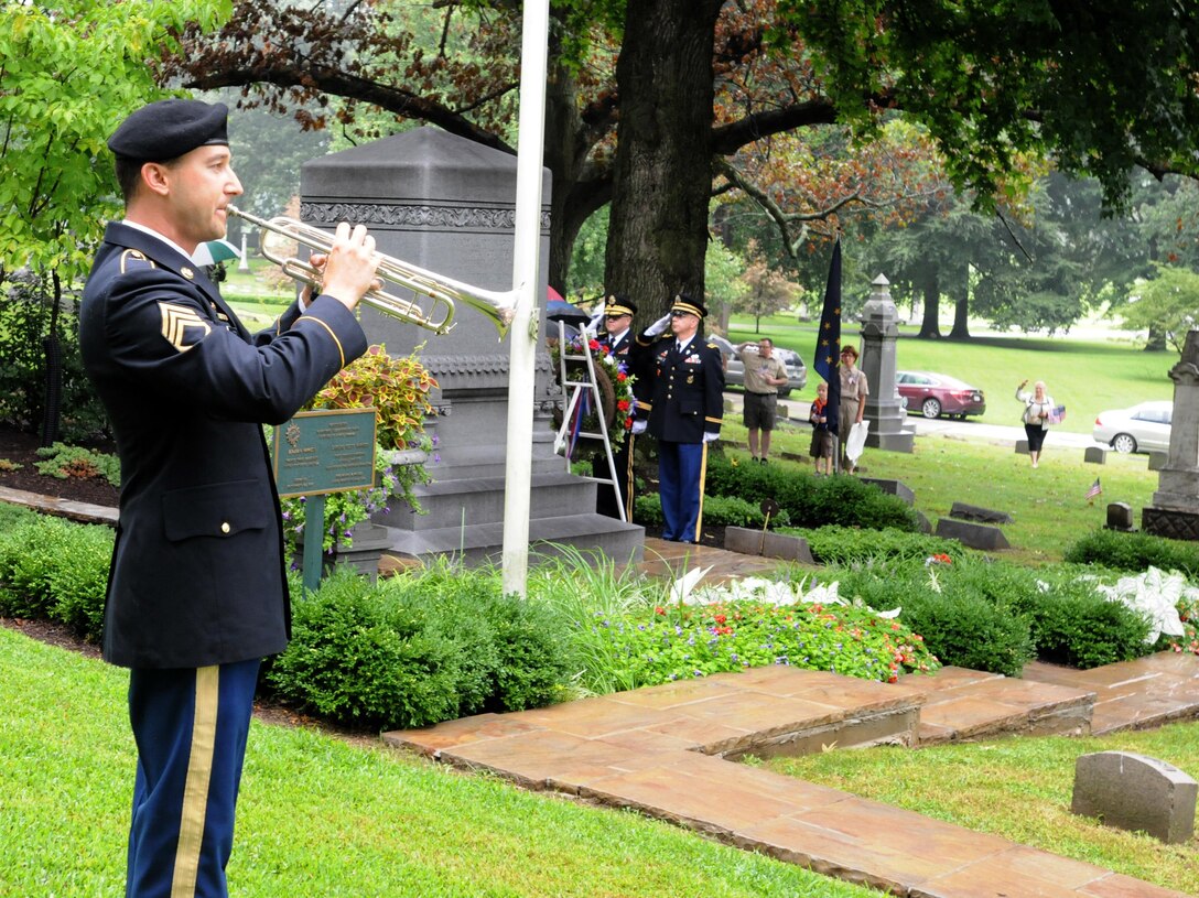 Staff Sgt. Jeff Hotz, a bugler with the 338th Army Band, plays taps during the President Benjamin Harrison wreath laying ceremony as Brig. Gen. Stephen E. Strand, back center, deputy commanding general, 88th Regional Support Command, and Chaplain (Maj.) Scott Hagen, deputy command chaplain, 88th RSC, salute the memorial, August 20.