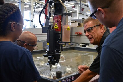 Mr. Ray Williams, 2nd from right, instructs Hull Maintenance Technician Fireman Mionna Green (L-R), Mr. Richard Cornwell and Hull Maintenance Technician 1st Class James Hampton on the intricacies of the cutting head. The cutter uses a 60,000 psi jet of water mixed with fine particles of garnet to cut steel and virtually any other material. Photo by Scott Curtis