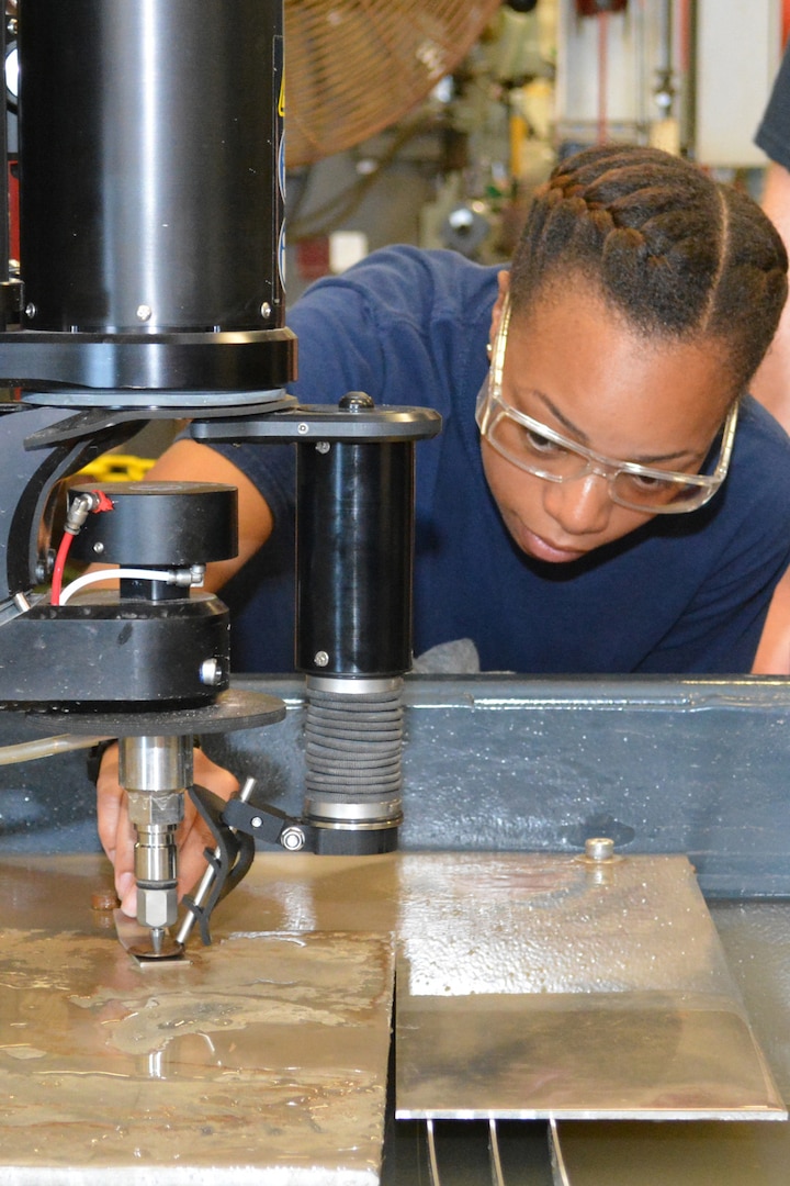 Hull Maintenance Technician Fireman Mionna Green adjusts the clearance of the cutting head on the new waterjet fabrication system at Southeast Regional Maintenance Center. Abrasive waterjet technologies enable the shipfitter shop here to cut components faster and more accurately, delivering them to the fleet more quickly and lowering overall production costs.