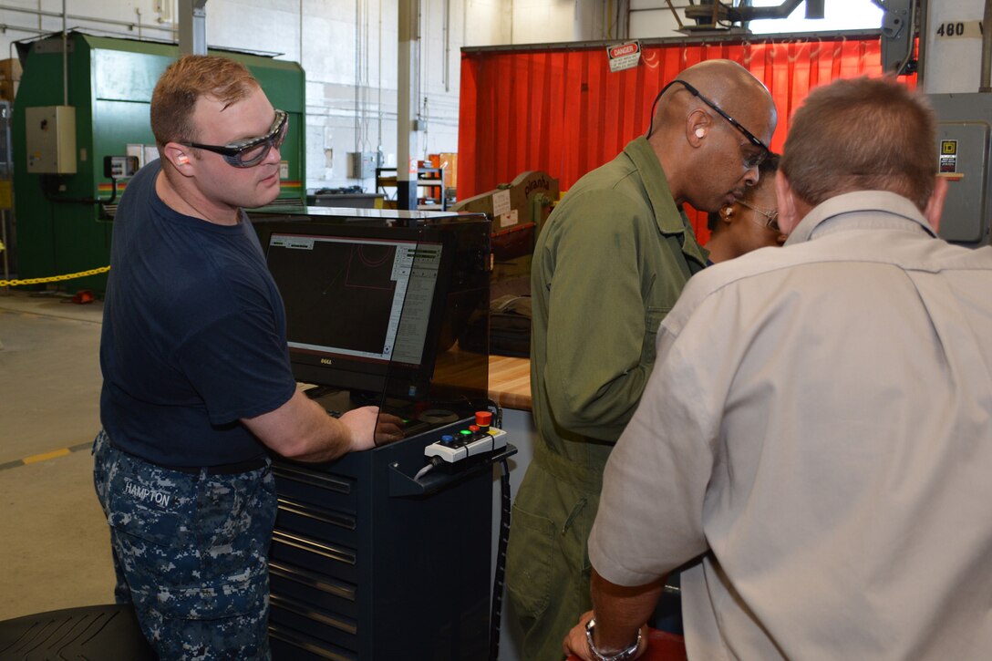 Hull Maintenance Technician 1st Class James Hampton directs the cutting head as (L-R) Mr. Richard Cornwell, Hull Maintenance Technician Fireman Mionna Green and Mr. Ray Williams observe. Abrasive waterjets can cut a wide-variety of materials with a nozzle delivering 60,000 psi of water and finely granulated garnet. Photo by Scott Curtis