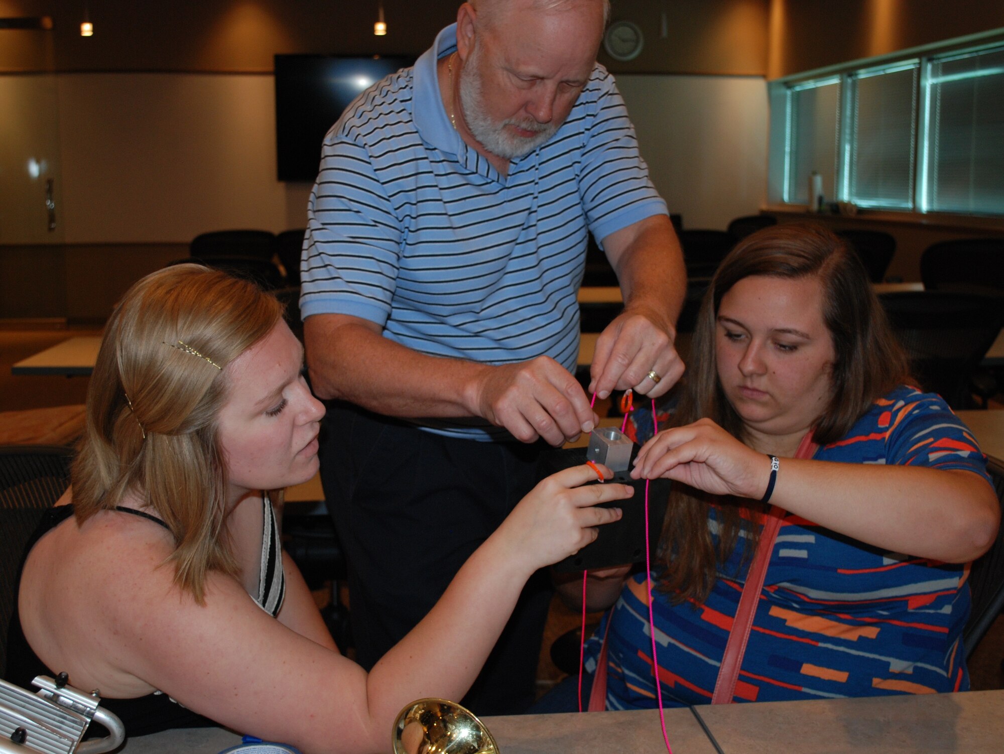 Kirsten Harmon (left) and Rachel Lavey, both recent Bradford High School graduates, work together with Robert Lee, Wright Brothers Institute engineer, to attach strings to the 3-D printed mounting device. The two students collaborated with WBI and the 711th Human Performance Wing to create a stand that could hold a trumpet for a Bradford Middle School student who has limited range of motion. (U.S. Air Force photo by Gina Marie Giardina)