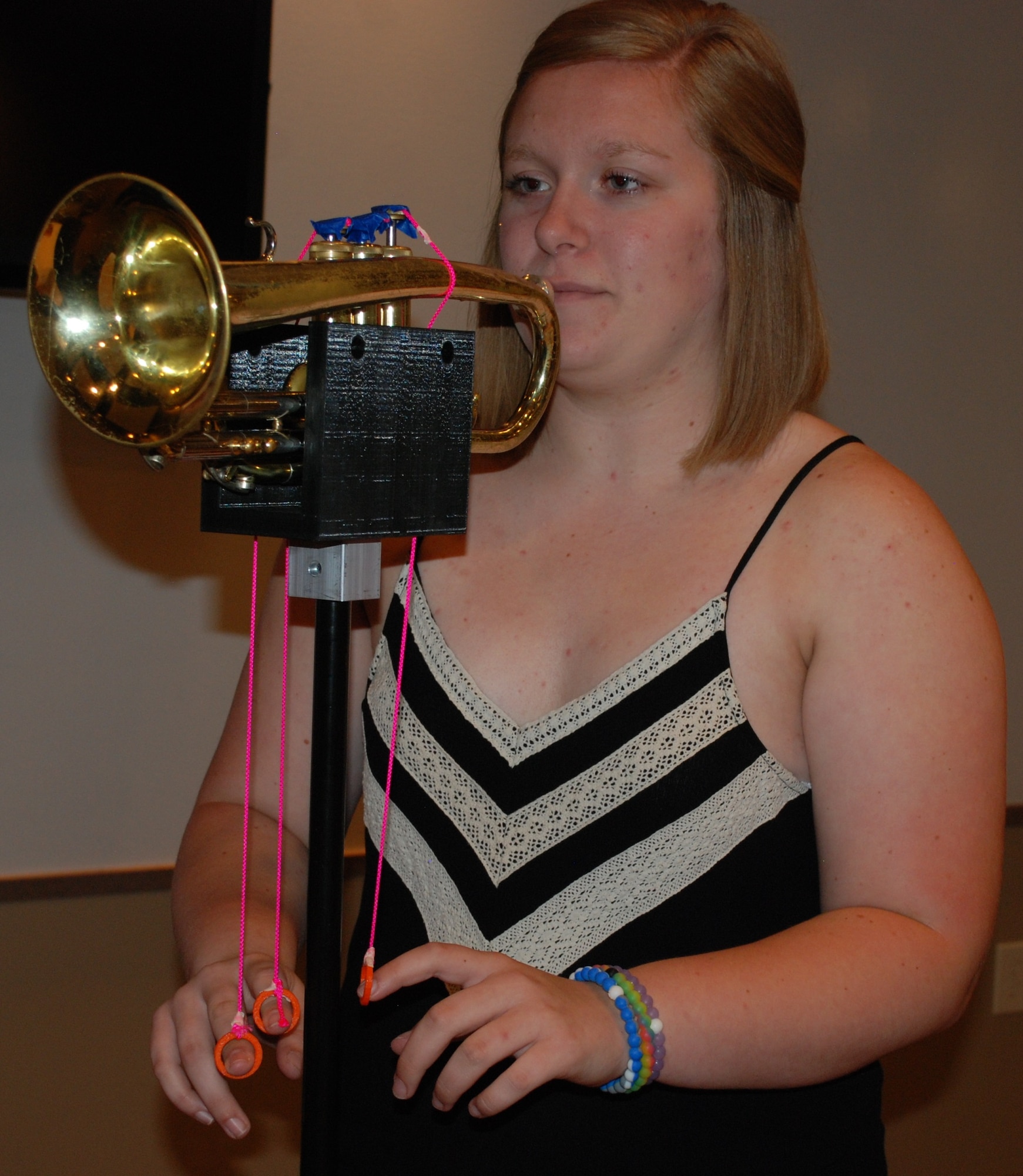Kirsten Harmon, a recent graduate from Bradford High School, demonstrates how the 3-D printed mounting device will hold the trumpet as well as how the student will be able to pull the strings to move the keys. Harmon and fellow classmate Rachel Lavey collaborated with WBI and the 711th Human Performance Wing to create the stand for a Bradford Middle School student with limited range of motion. (U.S. Air Force photo by Gina Marie Giardina)