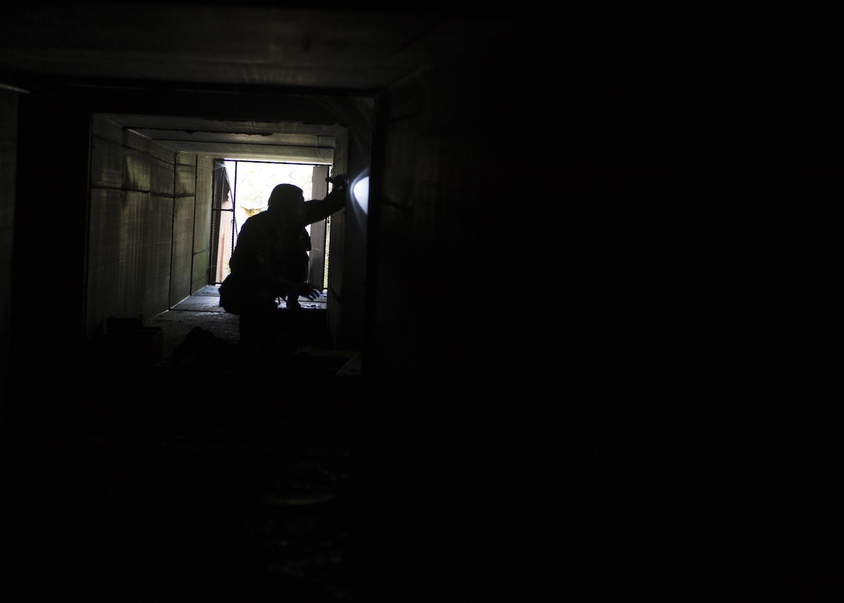 Tech. Sgt. Charles Hall, 512th Civil Engineer Squadron explosive ordinance disposal technician, shines a light down one of the tunnels in a simulated weapons cache during exercise Patriot Warrior, Aug. 17, 2016, Fort McCoy, Wis. The tunnel was lined with traps for Hall to diffuse during the exercise to test different EOD tactics. (U.S. Air Force Photo/ Tech. Sgt. Nathan Rivard)