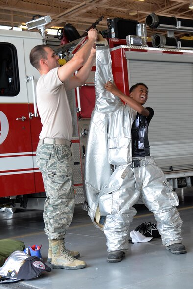Senior Airman Ian Morales, 47th Civil Engineer Squadron firefighter, helps a camper into his firefighting gear, during a week-long youth firefighting camp, on Laughlin Air Force Base, Texas, Aug. 16, 2016. The firefighting gear, or bunker gear, is used by firefighters to protect them from the intense heat of fires. (U.S. Air Force photo/Airman 1st Class Benjamin N. Valmoja)