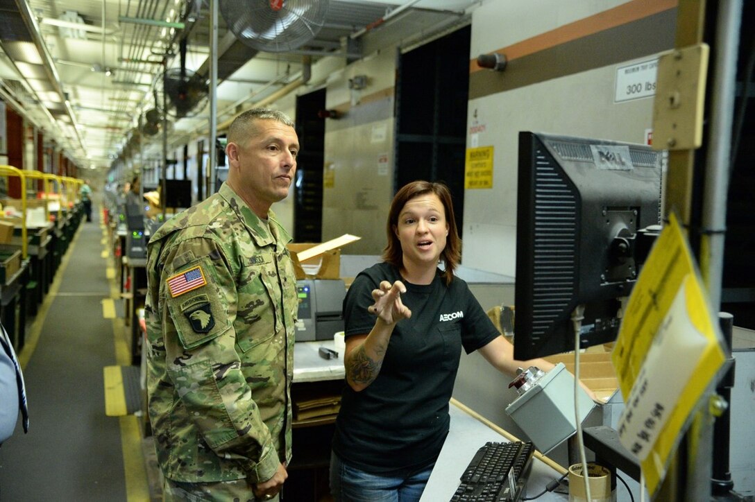Kandi Foy, shipping and receiving clerk at DLA Distribution Hill, Utah, is demonstrating the Distribution Standard System to Army Brig. Gen. John Laskodi, DLA Distribution commander, during his visit on Aug. 17.  Foy is showing how she performs the pick and stow functions in the Automated Storage Module.  