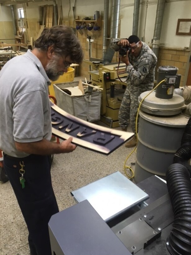 MUSCATATUCK, Ind.- U.S. Army Reserve Soldier Spc. Eddie Serra with the 205th Press Camp Headquarters takes photo of Bill LaFollette sanding and preparing a Ranger sign before applying a final coat of varnish.  LaFollette demonstrates his work at the Muscatatuck Urban Training Center Carpentry Shop in Butlerville, Ind., Aug. 22, 2016. (U.S. Army Photo by Capt. Cynthia Hernandez)