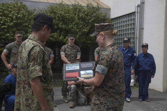 U.S. Marine Corps Sgt. Adrian Nanez, right,  Provost Marshal’s Office kennel master with Headquarters and Headquarters Squadron, presents a plaque to Japan Maritime Self-Defense Force Capt. Yasushi Fujita, left, JMSDF Kure area security command post chief, and JMSDF handlers during joint training at Marine Corps Air Station Iwakuni, Japan, Aug. 24, 2016. Handlers and their military working dogs train regularly in a variety of areas such as locating explosives, narcotics, conducting patrols and human tracking in order to become a more effective team. Upon completion of training, U.S. handlers presented a plaque to Fujita and JMSDF handlers as a sign of gratitude and willingness to continue strengthening the U.S. and Japan alliance. (U.S. Marine Corps photo by Lance Cpl. Jacob A. Farbo)
