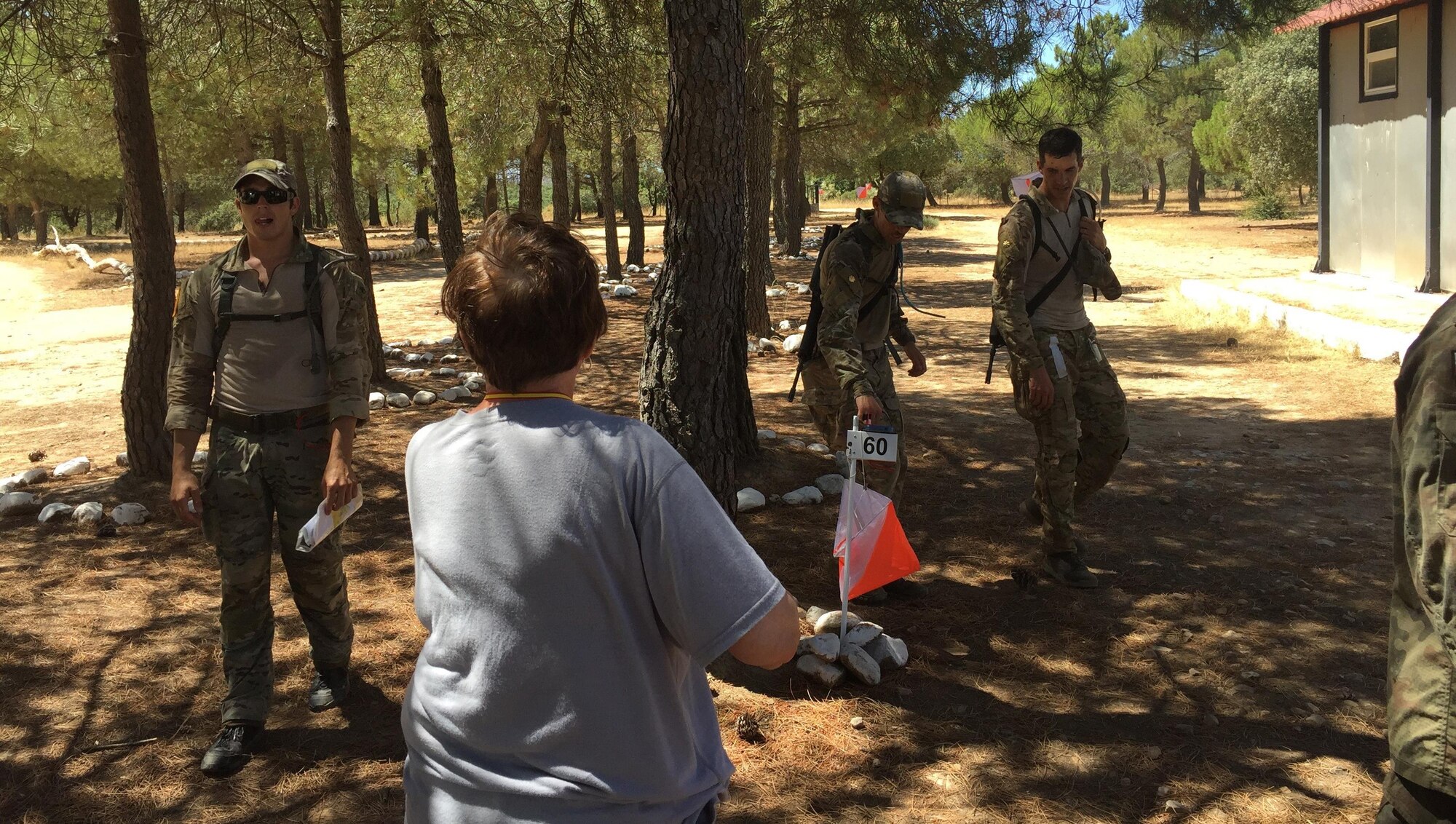 Linda Ferguson, Orienteering Coach, cheers USA Team 4 as they complete the grueling 13-kilometer Orienteering Course in 100-degree heat. (L to R): Staff Sgt. Matt Gaddy, Maj. Mike Masuda (using the electronic punch to record the team’s finish) and Maj. Pete Grossenbach.  