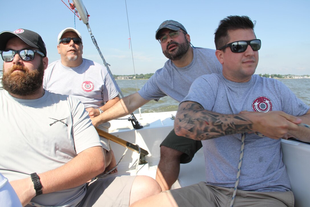 Army veteran James Hansen, left, watches the wind direction as Navy veteran and Valhalla sailing instructor Frank Briguglio surveys the skills of his new recruits during the Valhalla Sailing Project’s inaugural clinic to teach former military members the fundamentals of sailing and racing on the Chesapeake Bay in Annapolis, Maryland.  Marine Corps veteran Hector Cardona is at the tiller, and Marine Corps veteran Mike Wilson is adjusting the jib.
