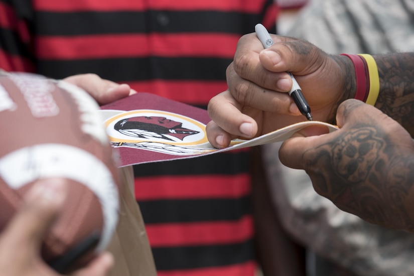 A Washington Redskins player signs a Redskins pennant during a preseason walk-through at Joint Base Andrews, Md., Aug. 25, 2016. The practice was followed by an autograph meet and greet with fans as a way for the Redskins to show their appreciation for the men and women of the armed forces. (U.S. Air Force Photo by Airman Gabrielle Spalding)