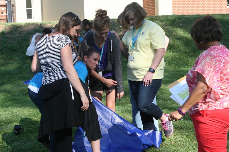 Teachers work together as teams to turn a tarp over without talking or allowing their feet to touch the ground, symbolizing the difficulties military children and spouses encounter when trying to integrate into a new community at a new duty station. This exercise was part of the "PCS Challenge," which was led by MCBQ and Fort Belvoir school liaisons to give educators an idea of what their military students go through when they move. This training was held Aug. 24 at Kyle Wilson Elementary School in Prince William County.