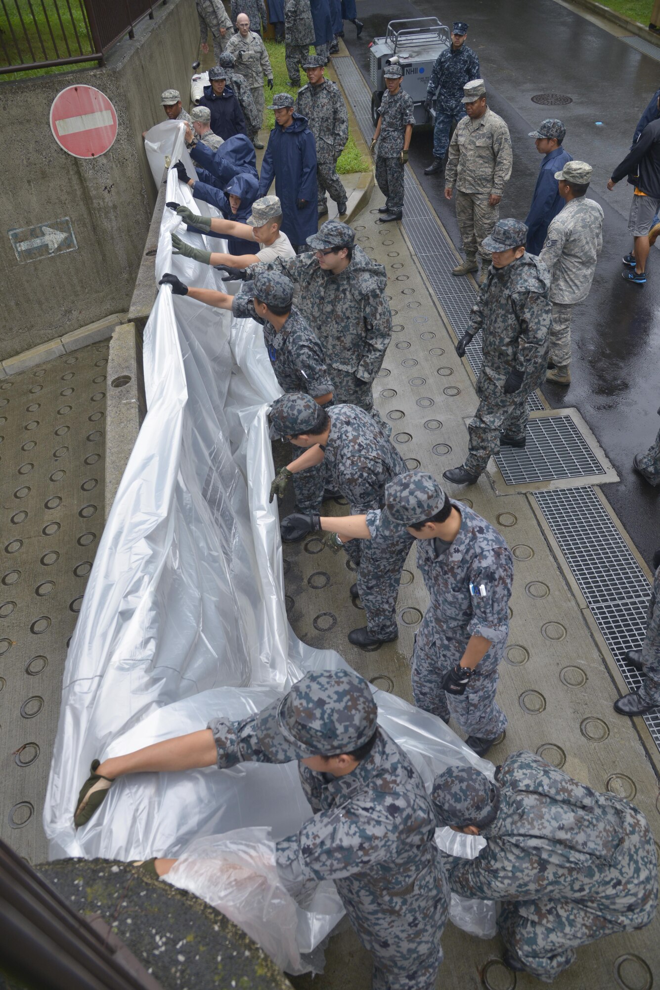 Airmen from Yokota Air Base work alongside Japan Air Self-Defense Force members to place a plastic tarp over cement barriers at the entrance of a tower’s basement pathway at Yokota Air Base, Japan, Aug. 29, 2016. The barriers were set up in preparation of potential flooding from an incoming typhoon. (U.S. Air Force photo by Senior Airman David Owsianka/Released)