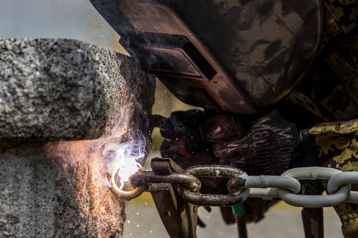 Petty Officer 2nd Class Kenneth Lancaster, a steel worker with Headquarters and Headquarters Squadron Facilities welds chains onto the 1st Marine Aircraft Wing Vietnam Memorial as part of a restoration project at Marine Corps Air Station Iwakuni, Japan, Aug. 17, 2016. The memorial, located next to the main side post office, contains a granite monument with 493 engraved names of Marines from the 1st MAW who died in action during the Vietnam War. Constructed in May 1972, the memorial has a black and red torii standing between it and the setting sun to honor the fallen, and symbolizes the friendship and support of our Japanese neighbors. (U.S. Marine Corps photo by Lance Cpl. Aaron Henson)
