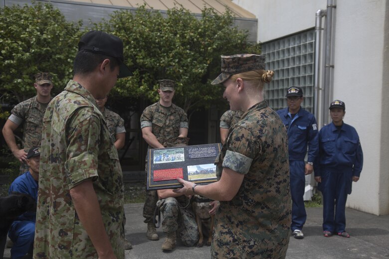 U.S. Marine Corps Sgt. Adrian Nanez, right,  Provost Marshal’s Office kennel master with Headquarters and Headquarters Squadron, presents a plaque to Japan Maritime Self-Defense Force Capt. Yasushi Fujita, left, JMSDF Kure area security command post chief, and JMSDF handlers during joint training at Marine Corps Air Station Iwakuni, Japan, Aug. 24, 2016. Handlers and their military working dogs train regularly in a variety of areas such as locating explosives, narcotics, conducting patrols and human tracking in order to become a more effective team. Upon completion of training, U.S. handlers presented a plaque to Fujita and JMSDF handlers as a sign of gratitude and willingness to continue strengthening the U.S. and Japan alliance. (U.S. Marine Corps photo by Lance Cpl. Jacob A. Farbo)