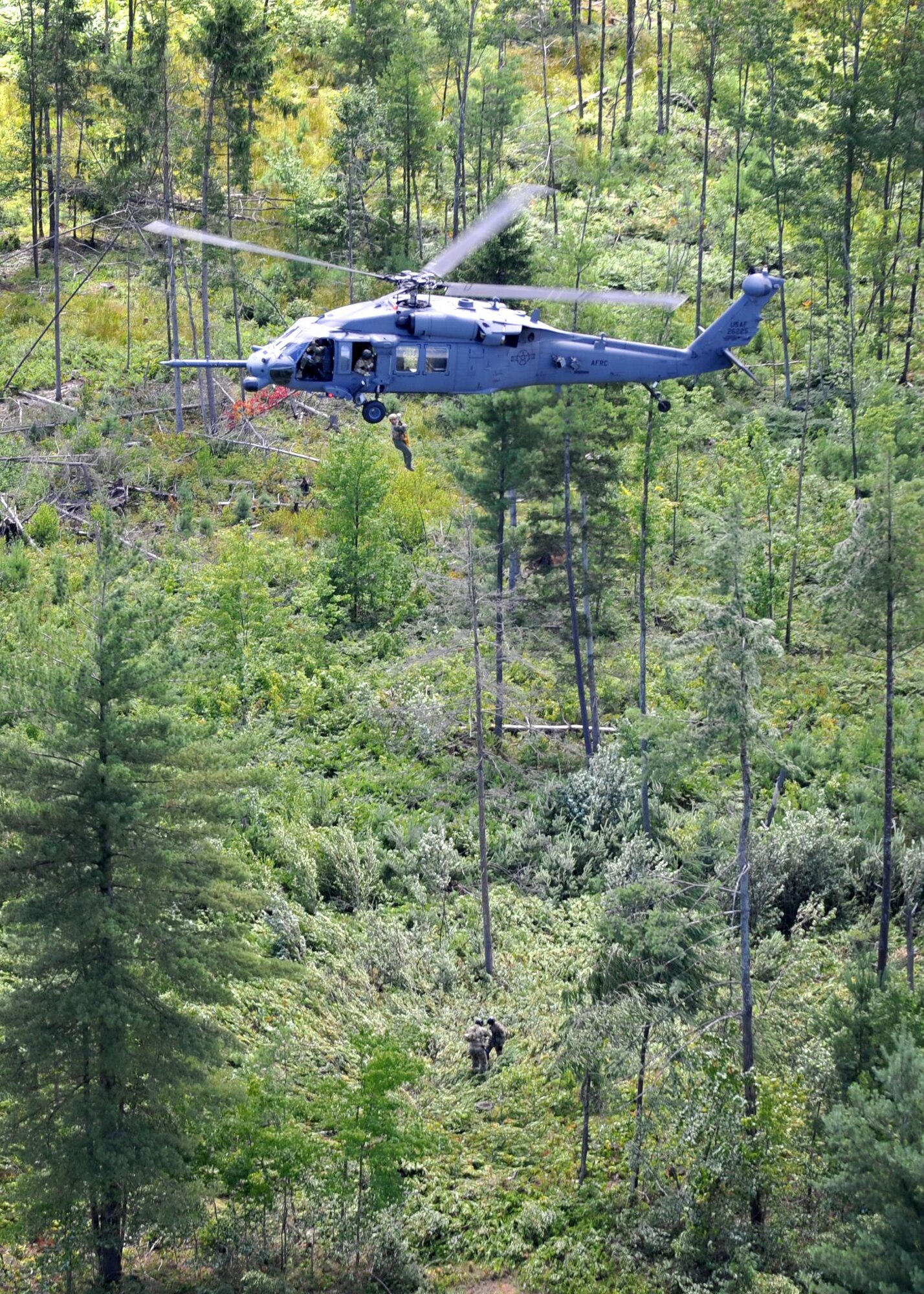 Air Force Reserve aircrew from the 943rd Rescue Group at Davis-Monthan Air Force Base, Ariz., hoist a (simulated) crash "survivor" out of the woods during a combat search and rescue training flight in upstate New York Aug. 2 while Tech. Sgt. Gary Waltz and Staff Sgt. Erik Wieland, two 306th Rescue Squadron SERE (Survive, Evade, Resist, Escape) specialists (pictured on the ground) assist the "survivor" in evading the opposing forces role players. As a part of the Guardian Angels, SERE specialists assist with recovery of isolated personnel. (U.S. Air Force photo by Carolyn Herrick)